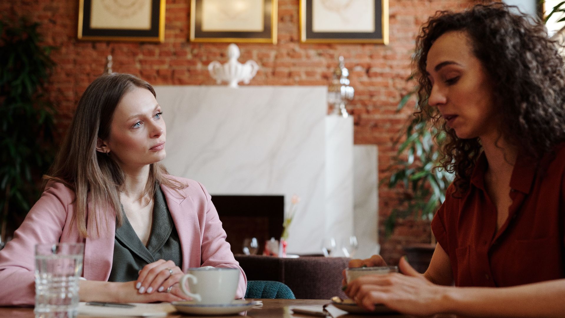 Two women engaged in serious discussion over coffee in a cozy indoor café setting.