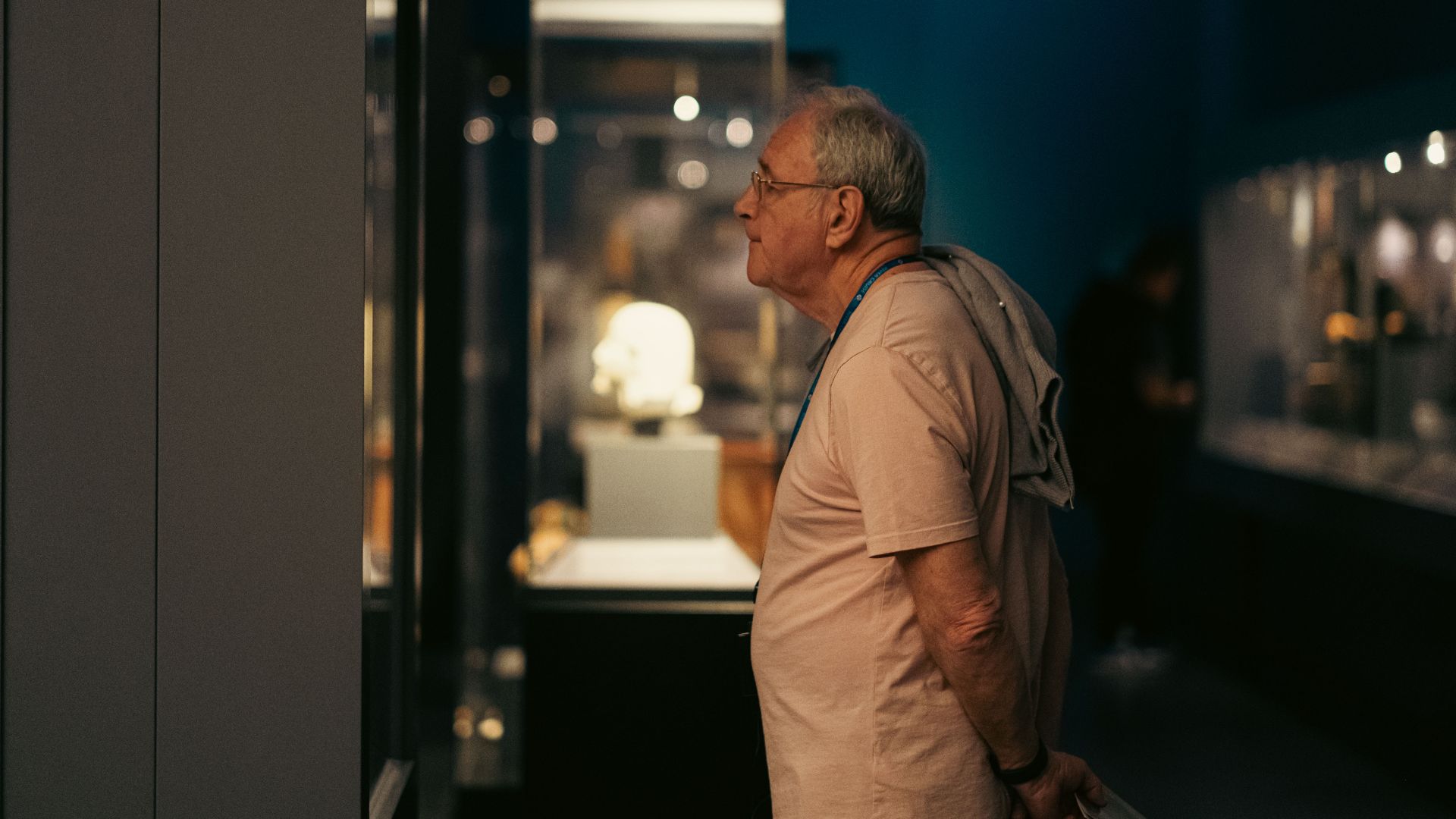 A senior man attentively explores exhibits in a dimly lit Budapest museum.