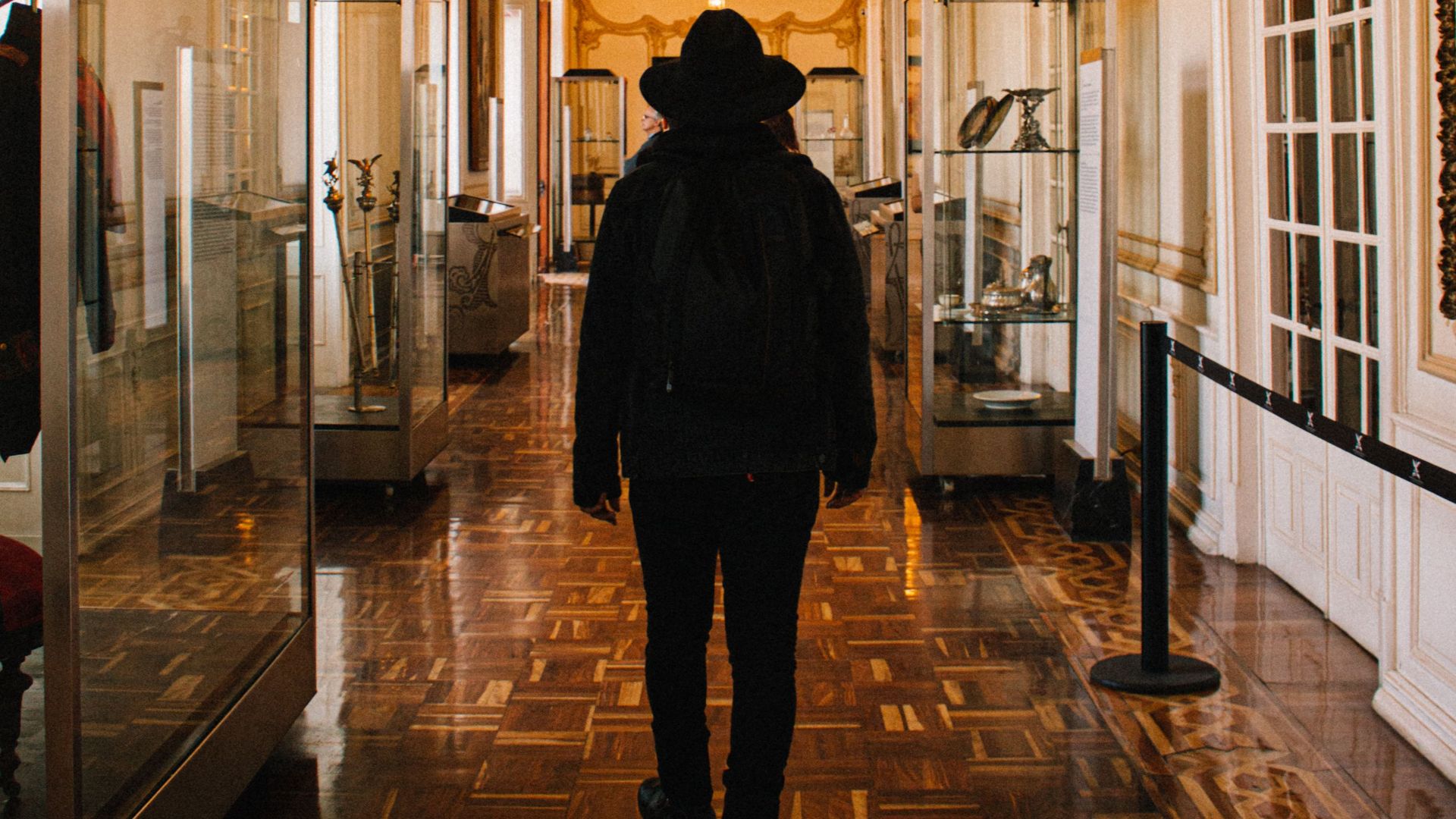 A man with a backpack walks through a luxurious, ornately decorated museum hallway.