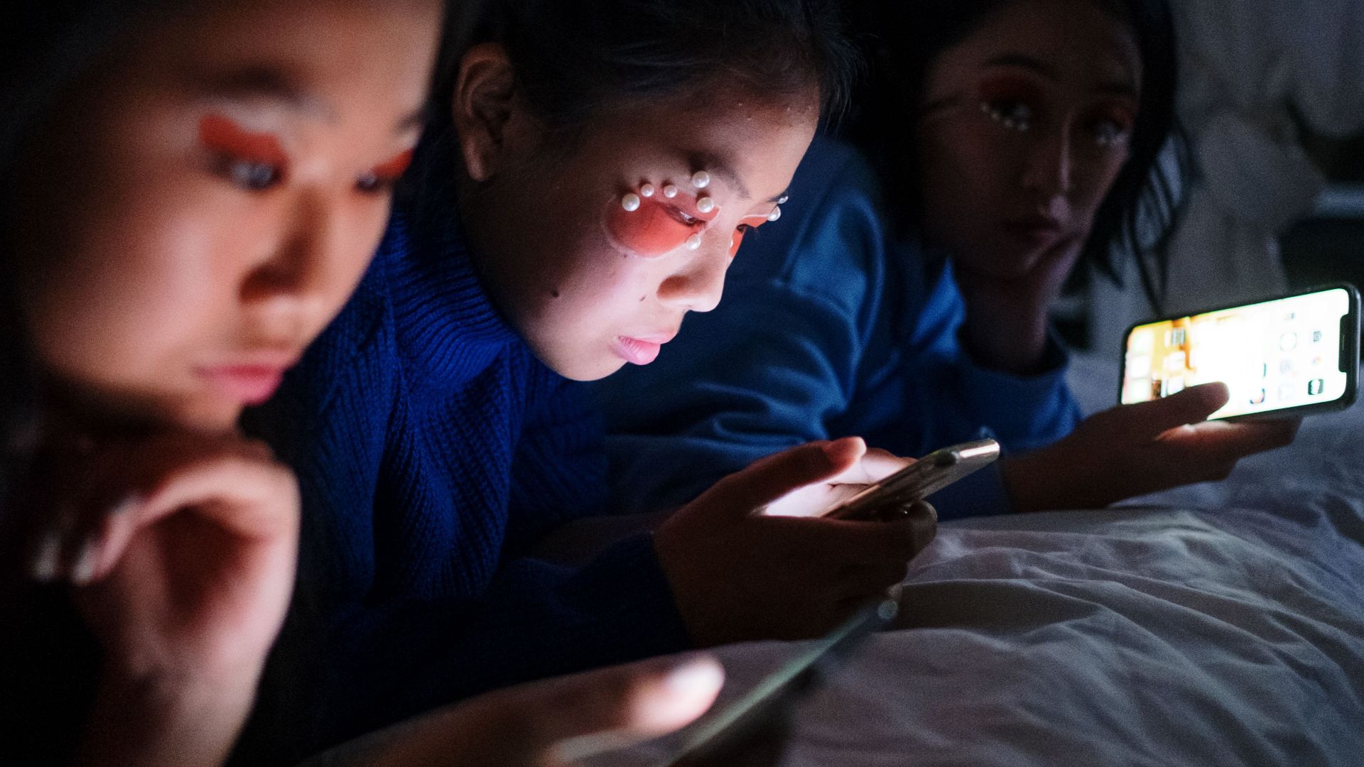 Three young women using smartphones in a dimly lit room at night.