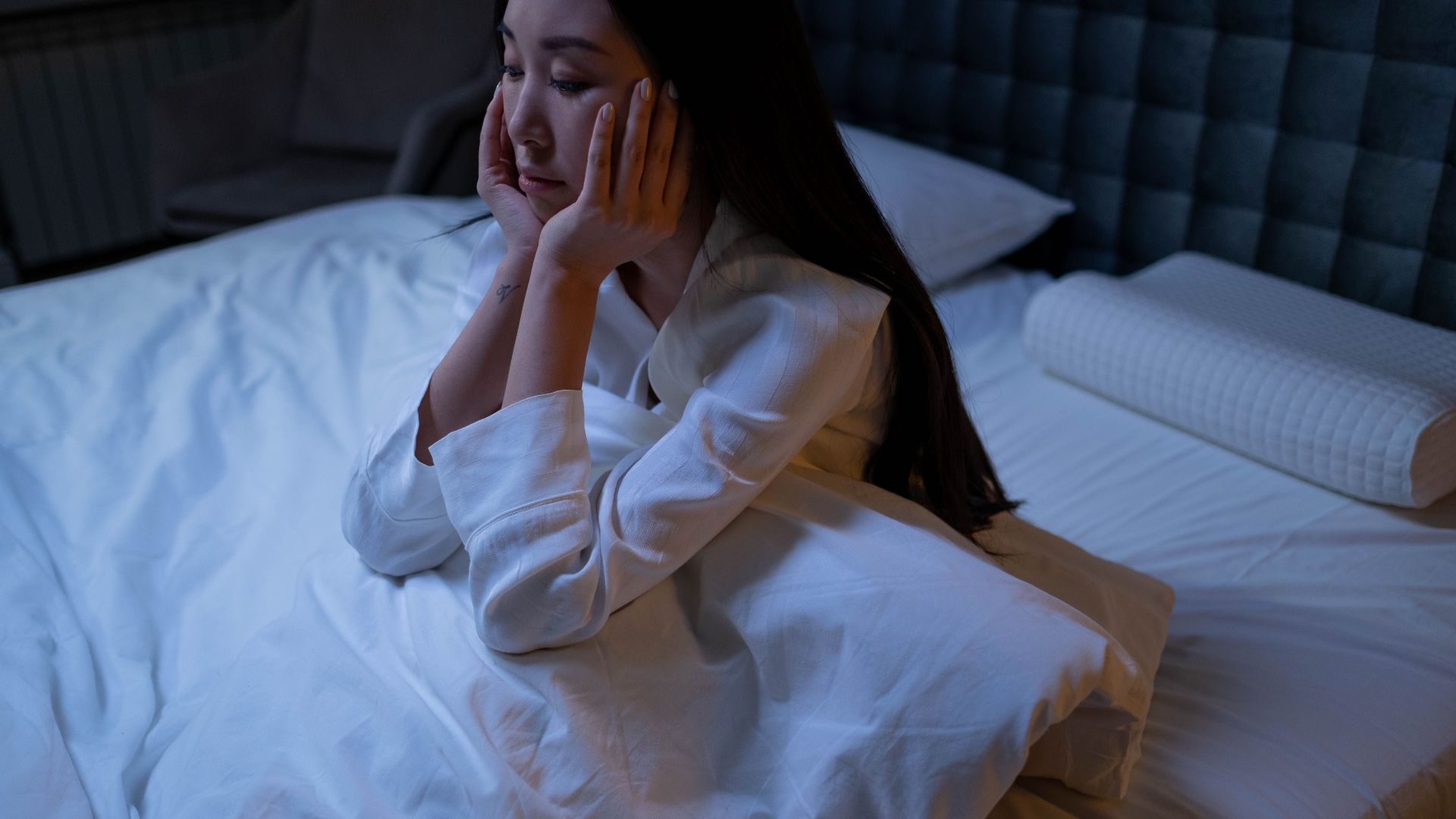 An Asian woman in bed at night, experiencing insomnia and loneliness, deep in thought.