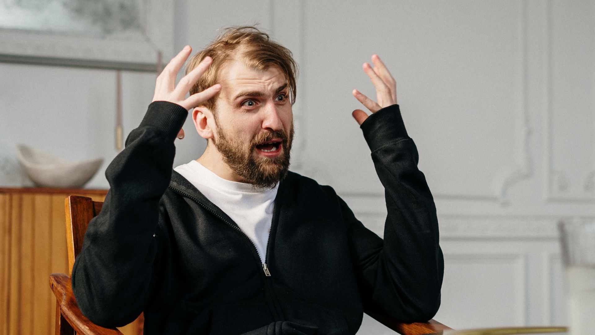 A man in a therapy session expressing emotions, seated indoors at a modern office.