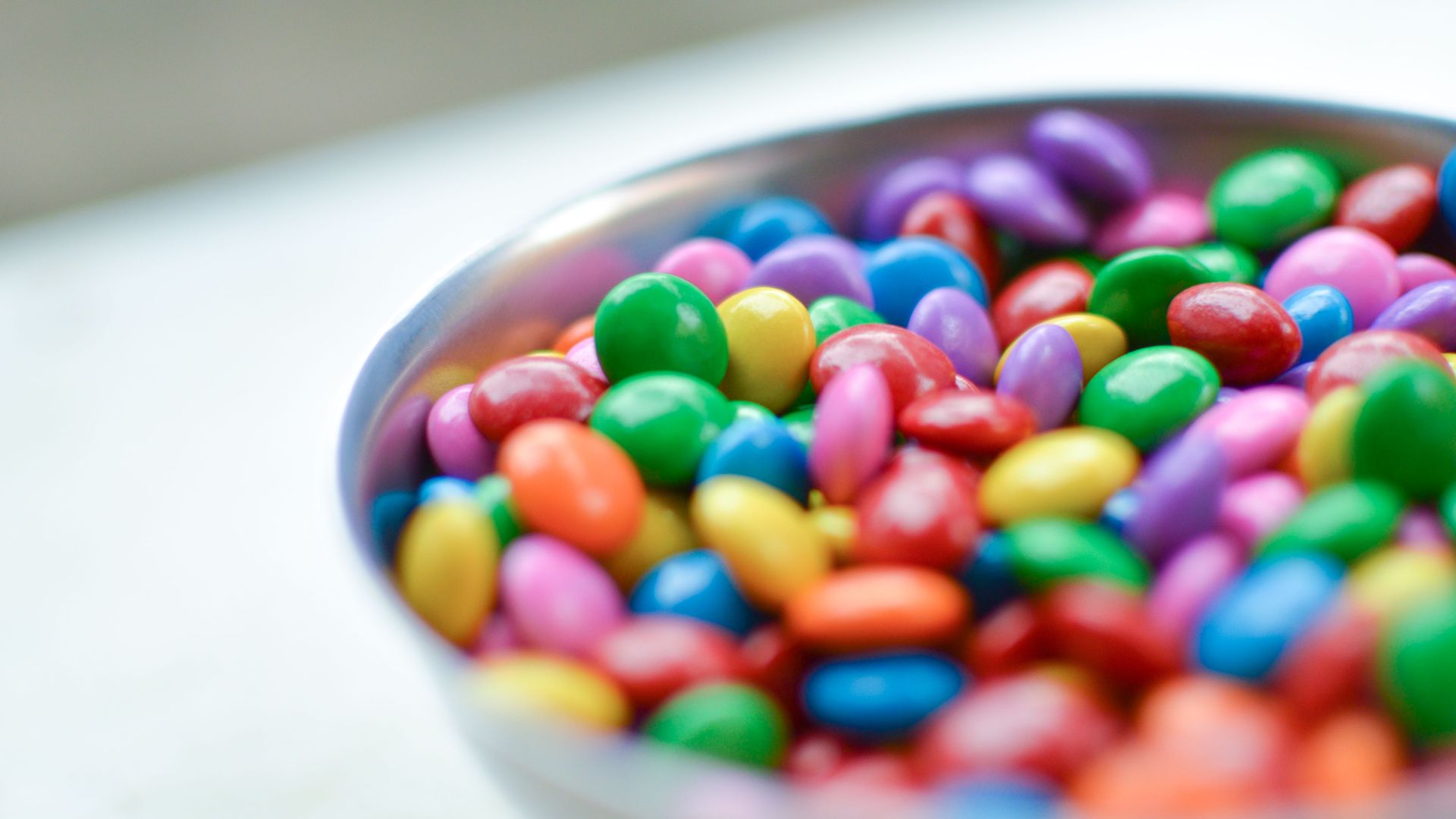 Vibrant close-up of assorted candy-coated chocolates in a silver bowl.