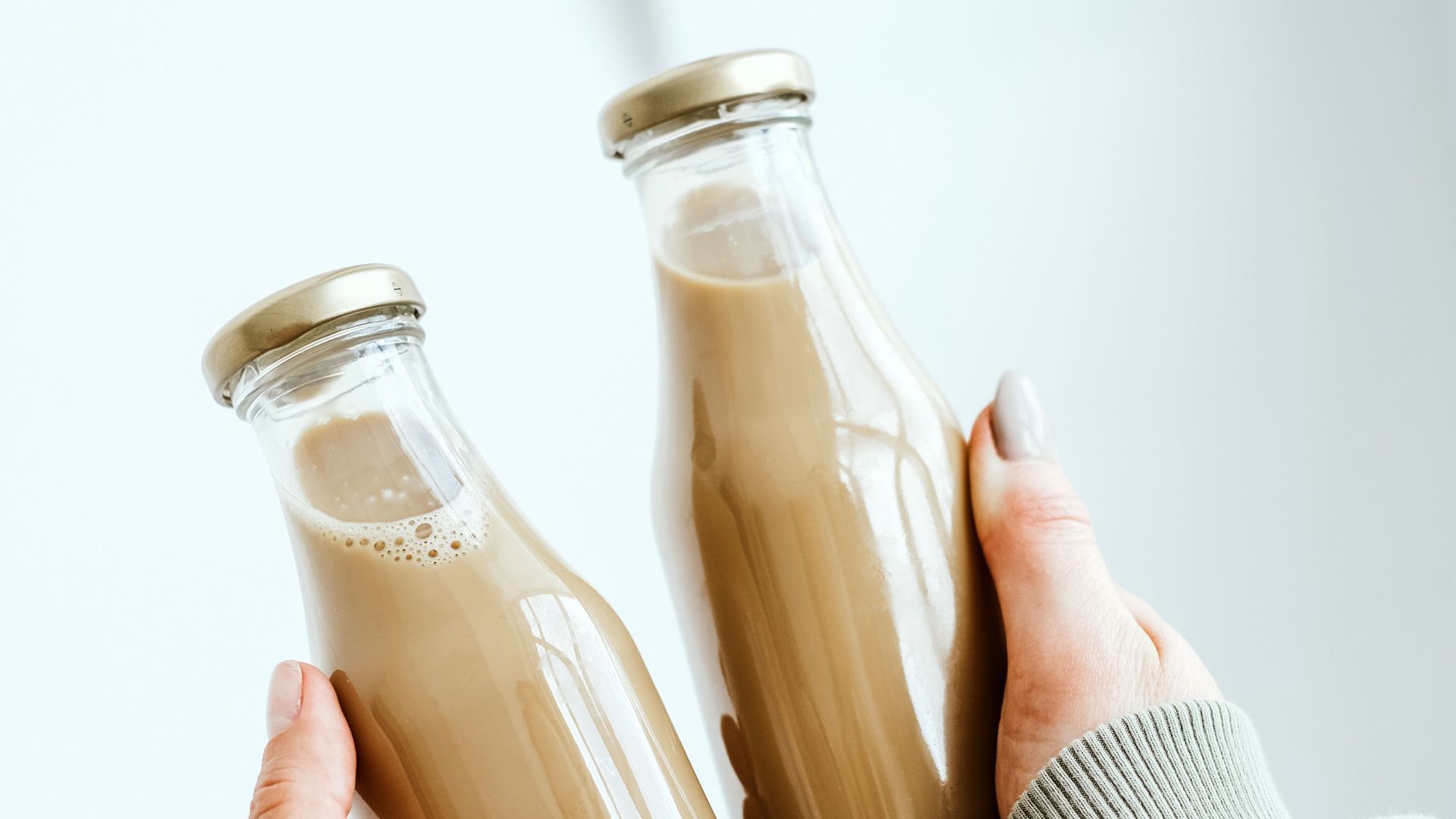 Two hands holding glass bottles of coffee against a minimalist backdrop, perfect for concepts of sharing and simplicity.