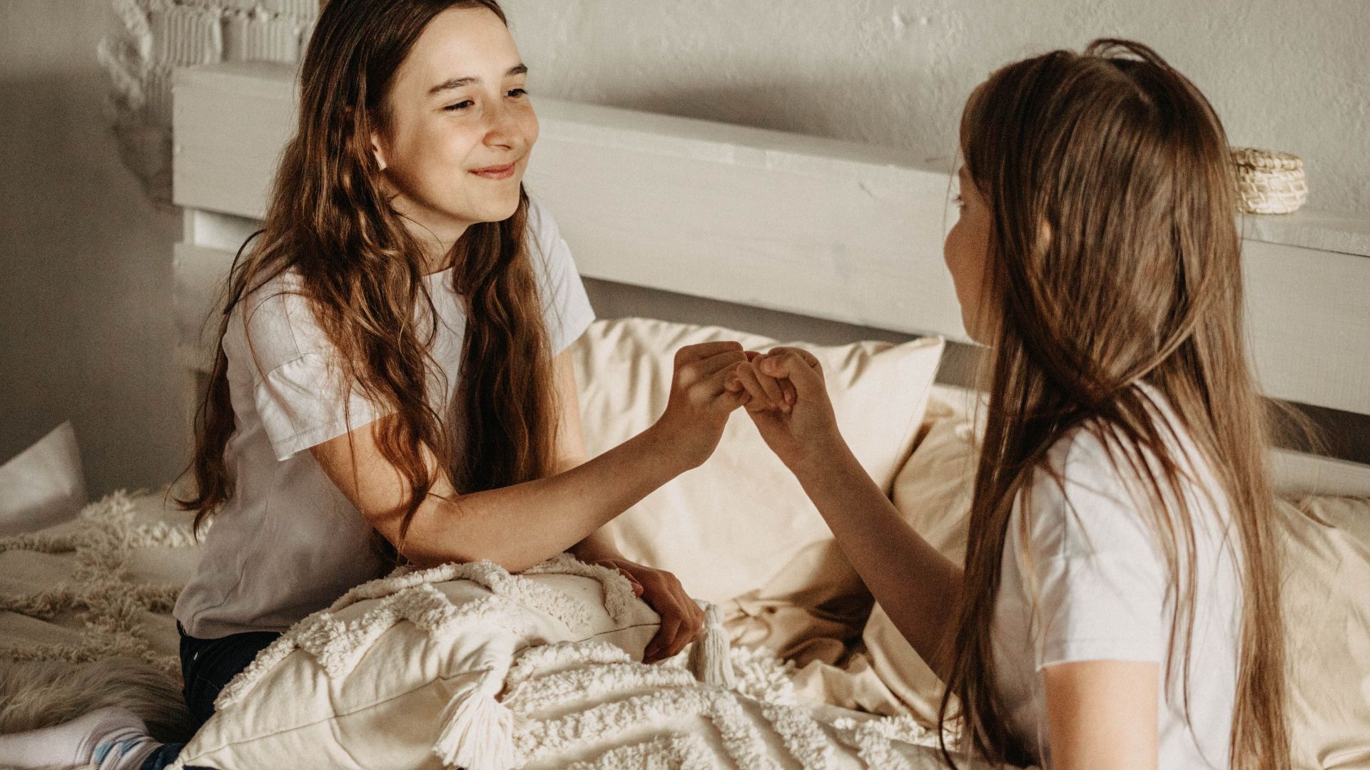 Teenage girls sitting on bed, engaged in a happy and serene moment of friendship.