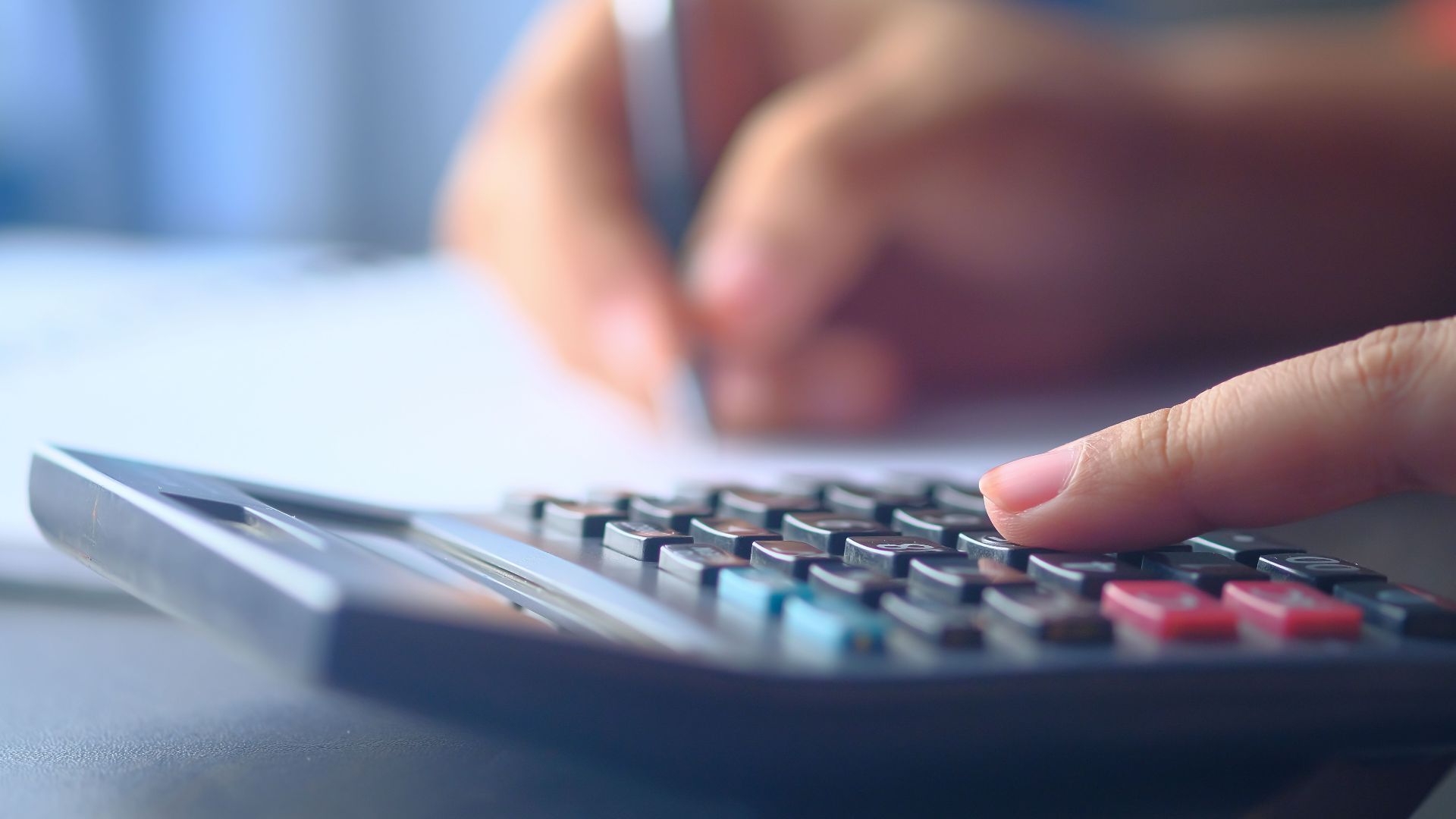 A close-up image of hands working on a calculator and writing, representing budgeting and financial planning.
