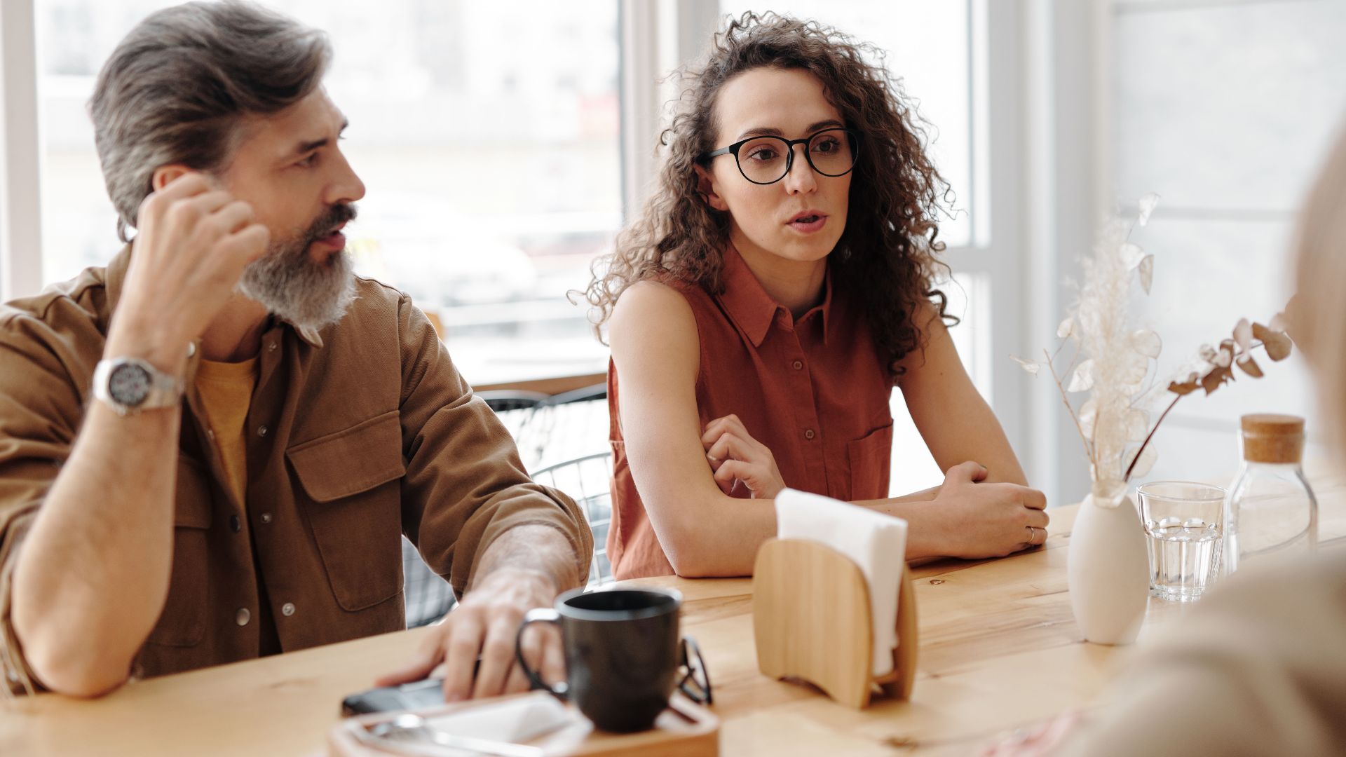 Adults in conversation at a coffee shop sharing ideas and companionship.