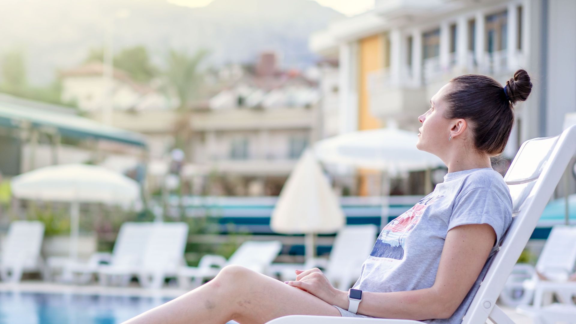 A woman enjoying leisure time on a sun lounger at a poolside resort during summer.
