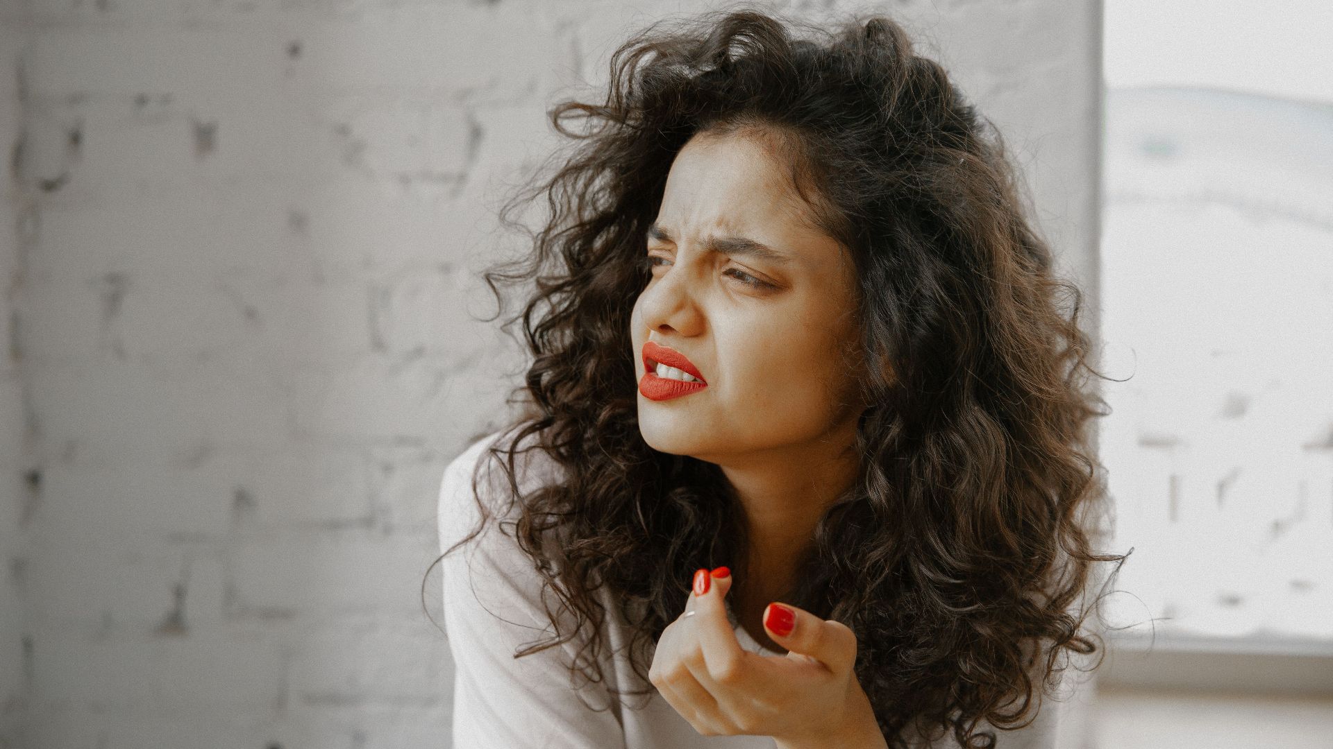 A brunette woman showing an expression of disgust against a brick wall.