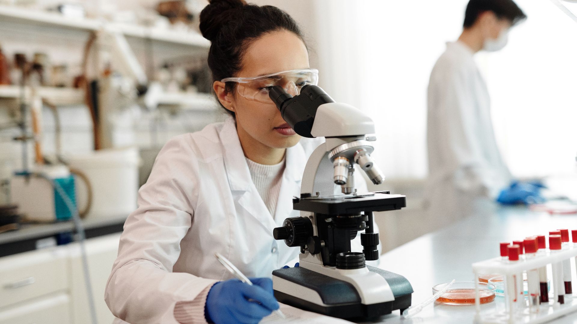 A scientist in a lab coat using a microscope in a modern laboratory setting.
