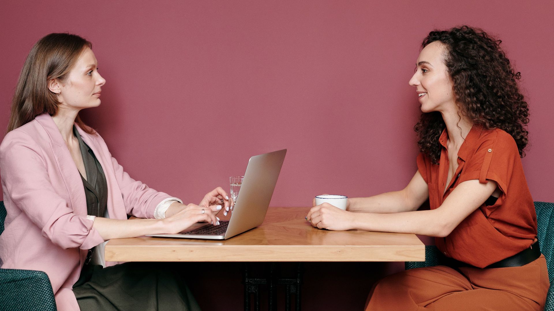 Two women having a meeting at a table with a laptop and coffee inside a stylish room.