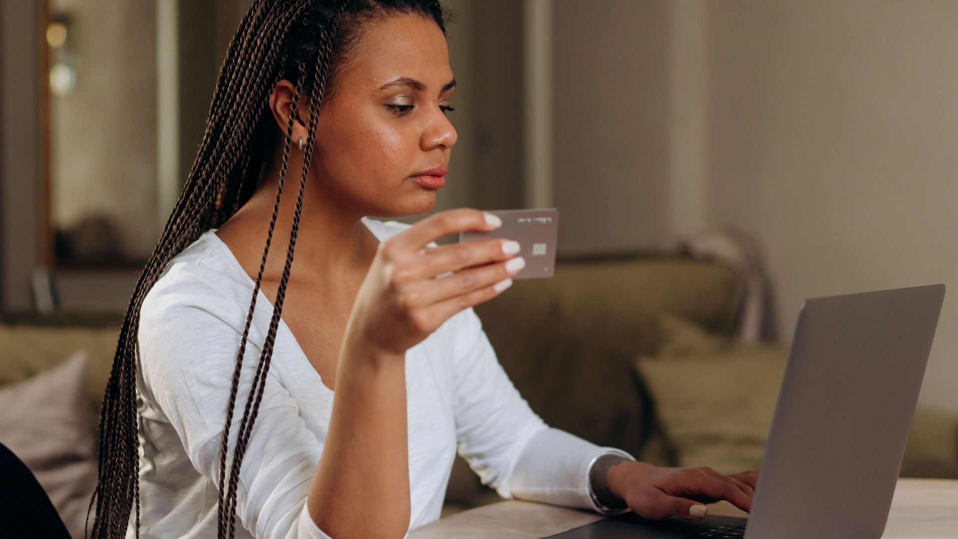 A woman with braided hair makes an online transaction using a credit card and laptop at home.