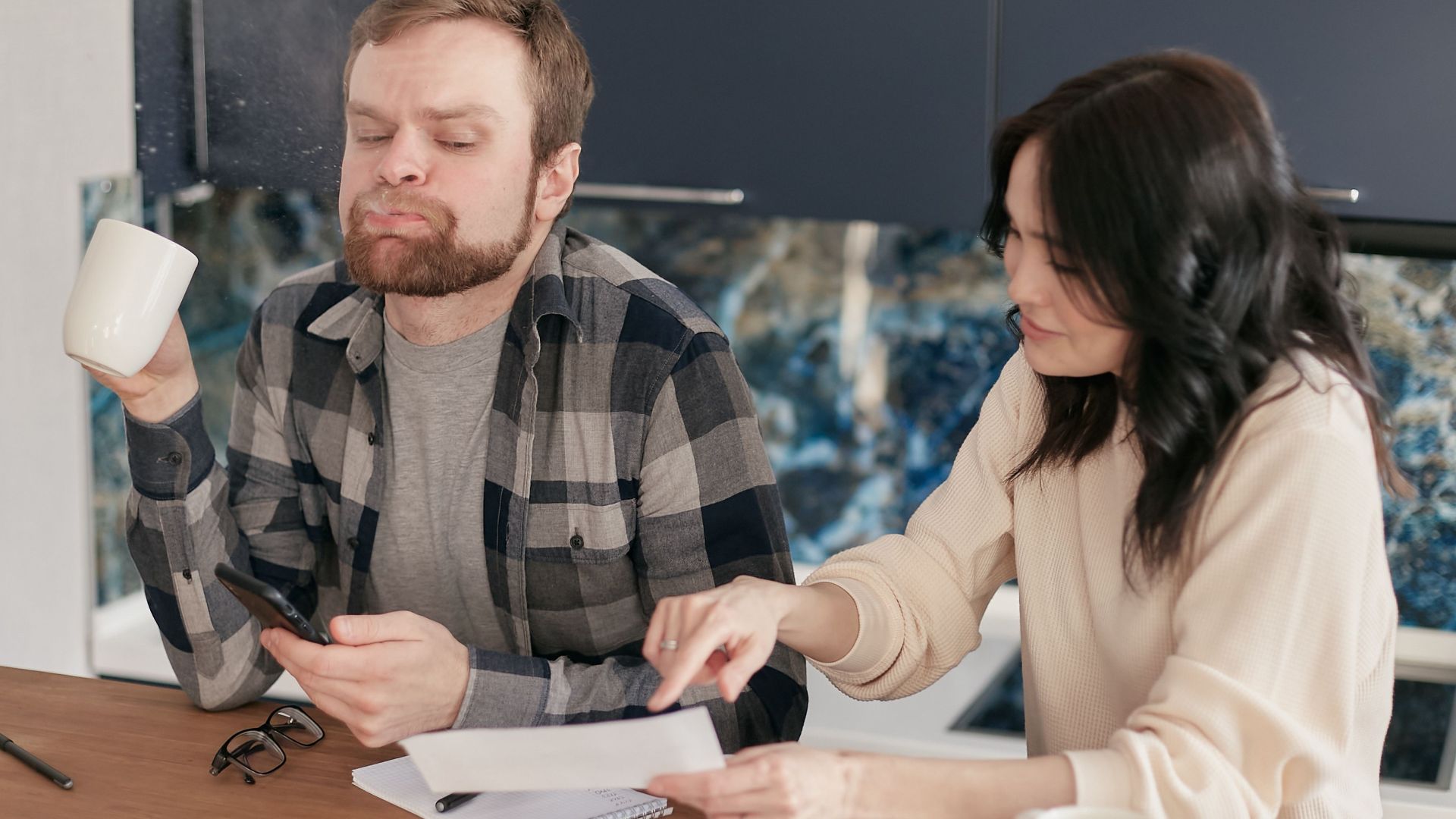 A couple reviews bills at their kitchen table, looking concerned and thoughtful.