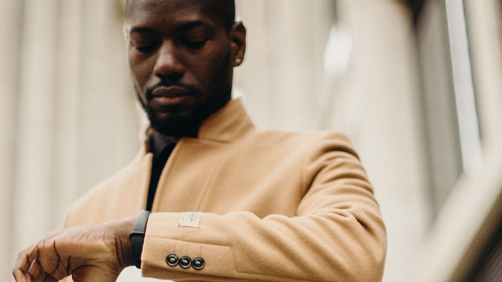 A fashionable businessman checks his watch while holding a laptop outdoors, showcasing a stylish urban vibe.