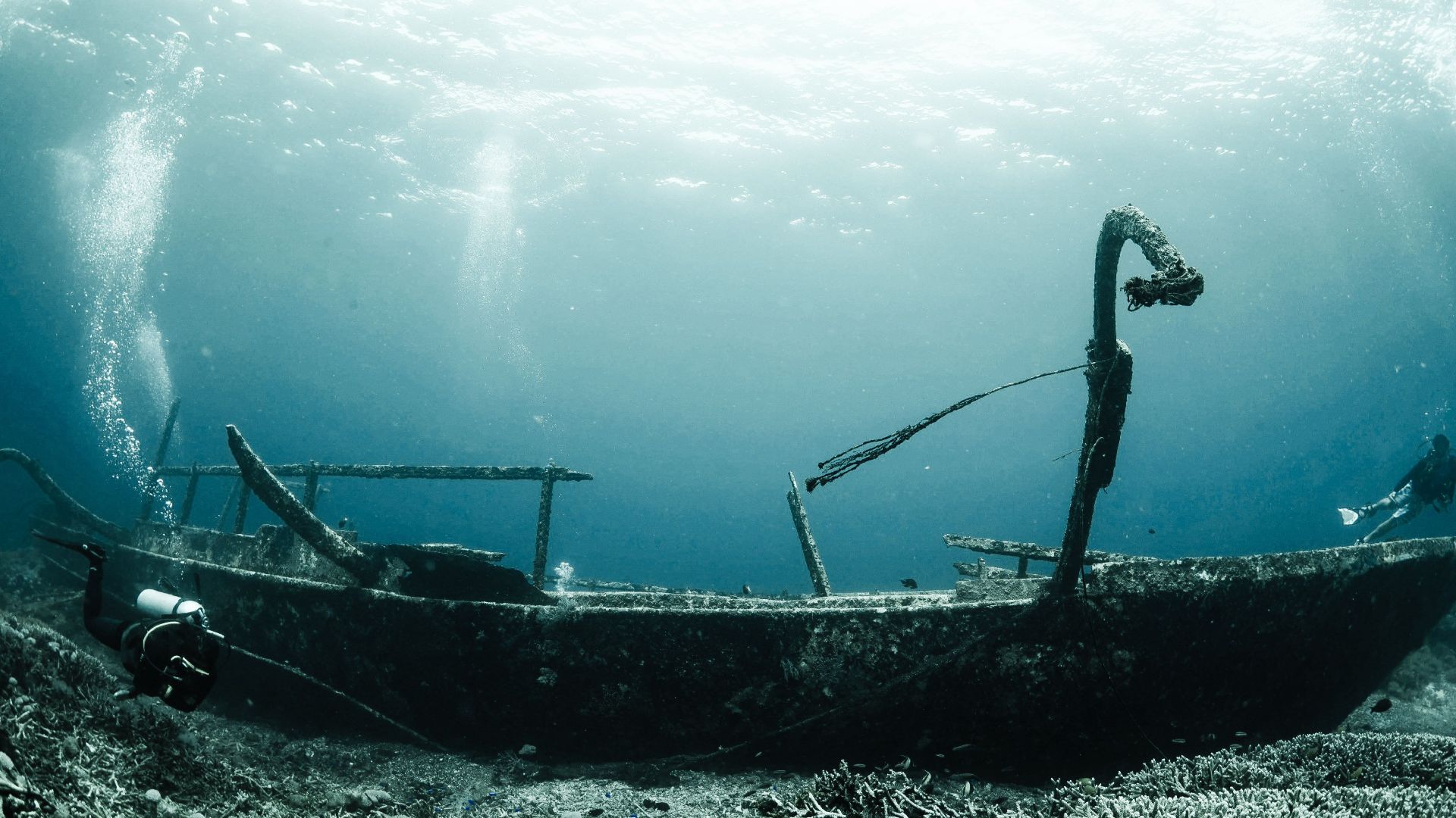 Explore a mysterious shipwreck underwater with scuba divers capturing the serene beauty of the deep blue sea.
