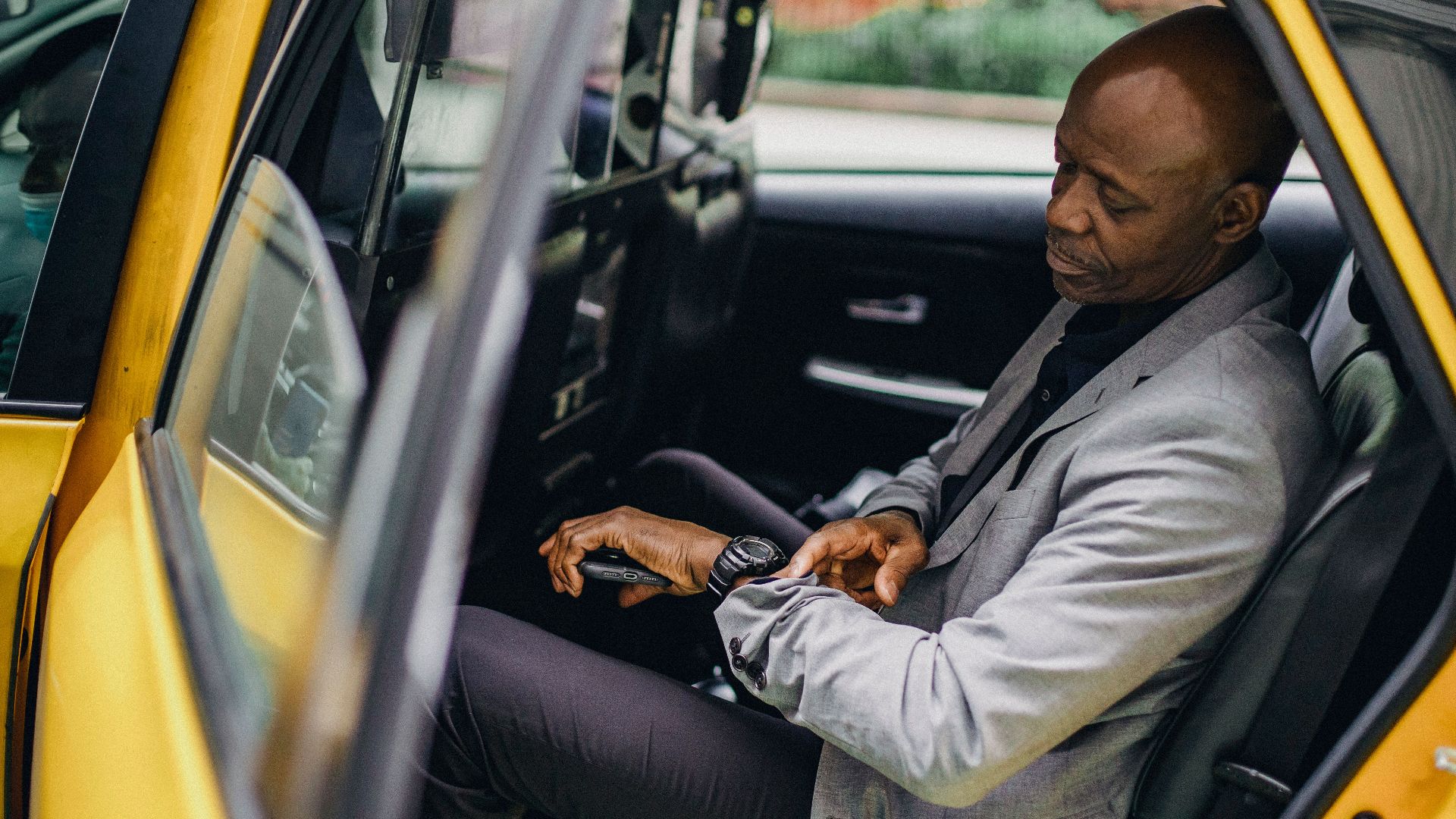 Side view punctual African American male wearing formal suit sitting in taxi back seat and checking time on wristwatch