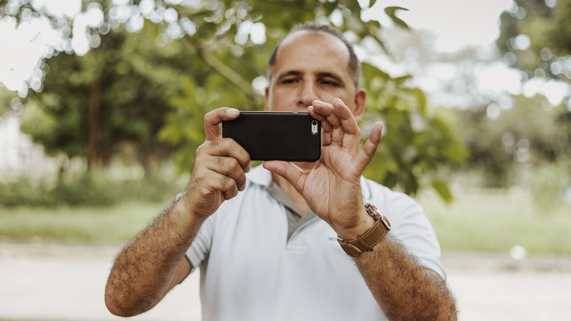 Adult man using smartphone to take a photo in a natural setting, showcasing modern technology and leisure.