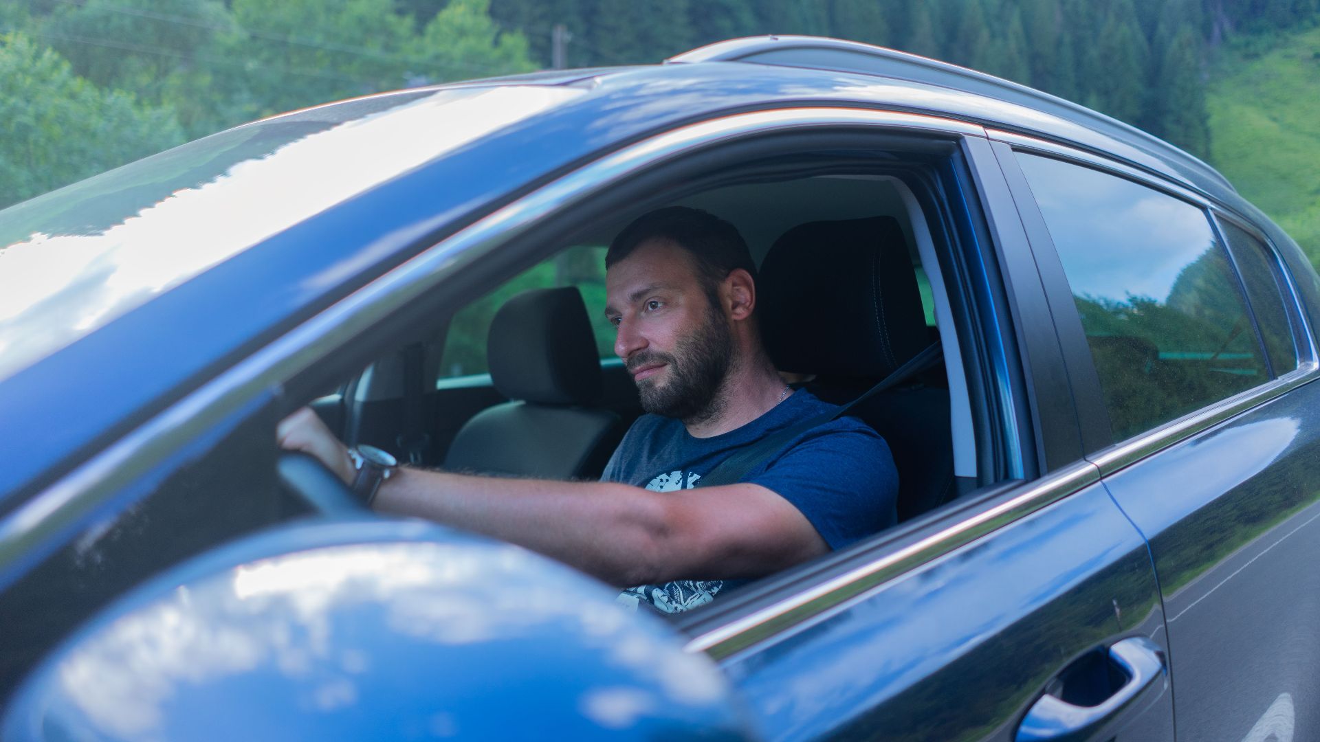 Bearded man enjoying a drive through lush green countryside on a sunny day.
