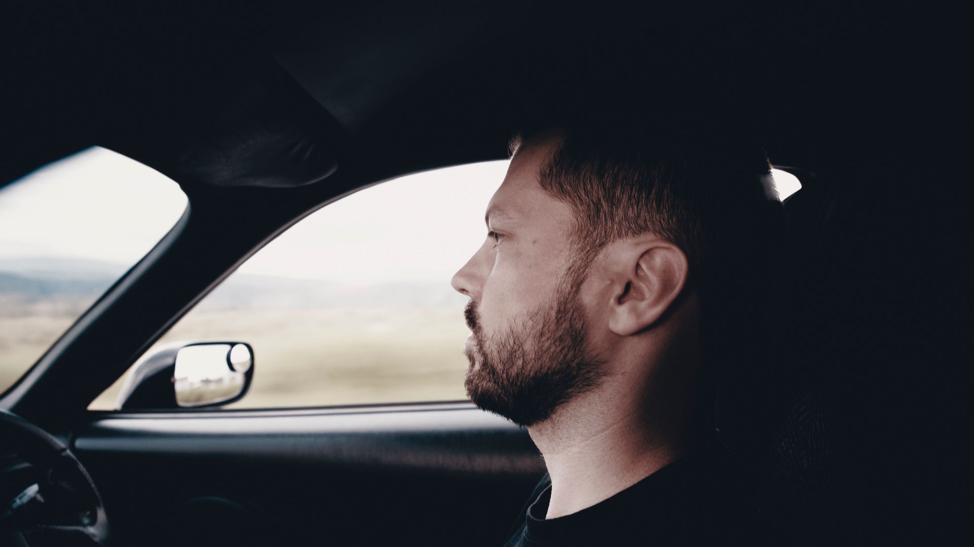 Side profile of a bearded man driving a car, focused and intent on the road.