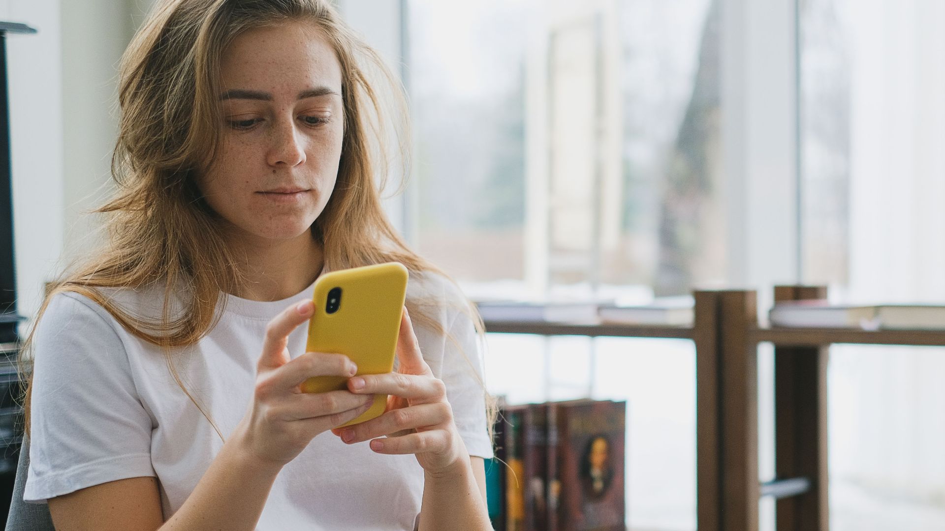 Young woman multitasking with smartphone and laptop in a cozy indoor setting.