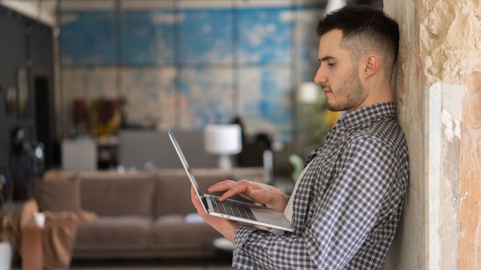 Man working on a laptop standing indoors with a modern office background. Ideal for business and technology themes.