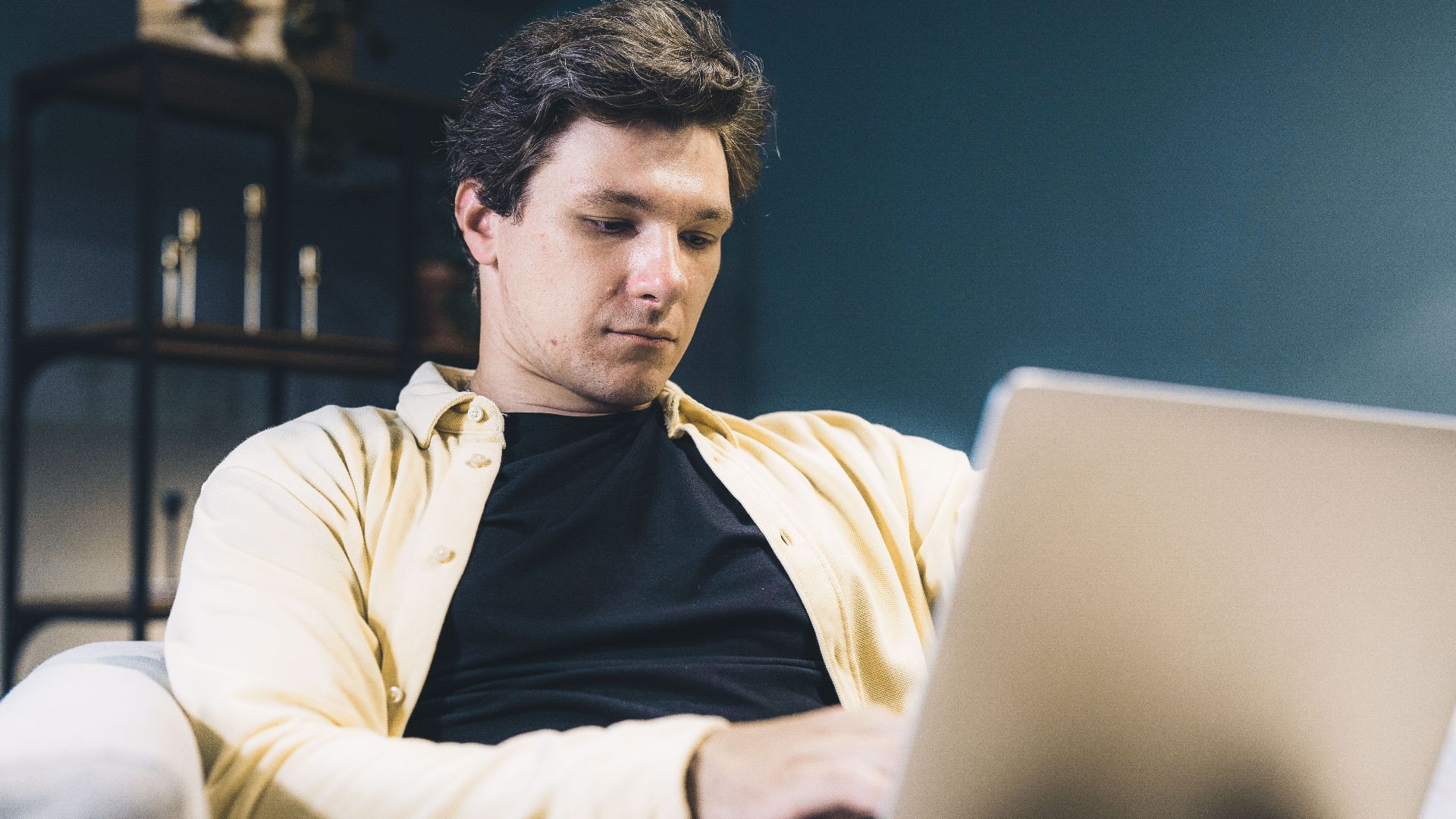 Focused young man sitting comfortably using a laptop at home, engaging in remote work.