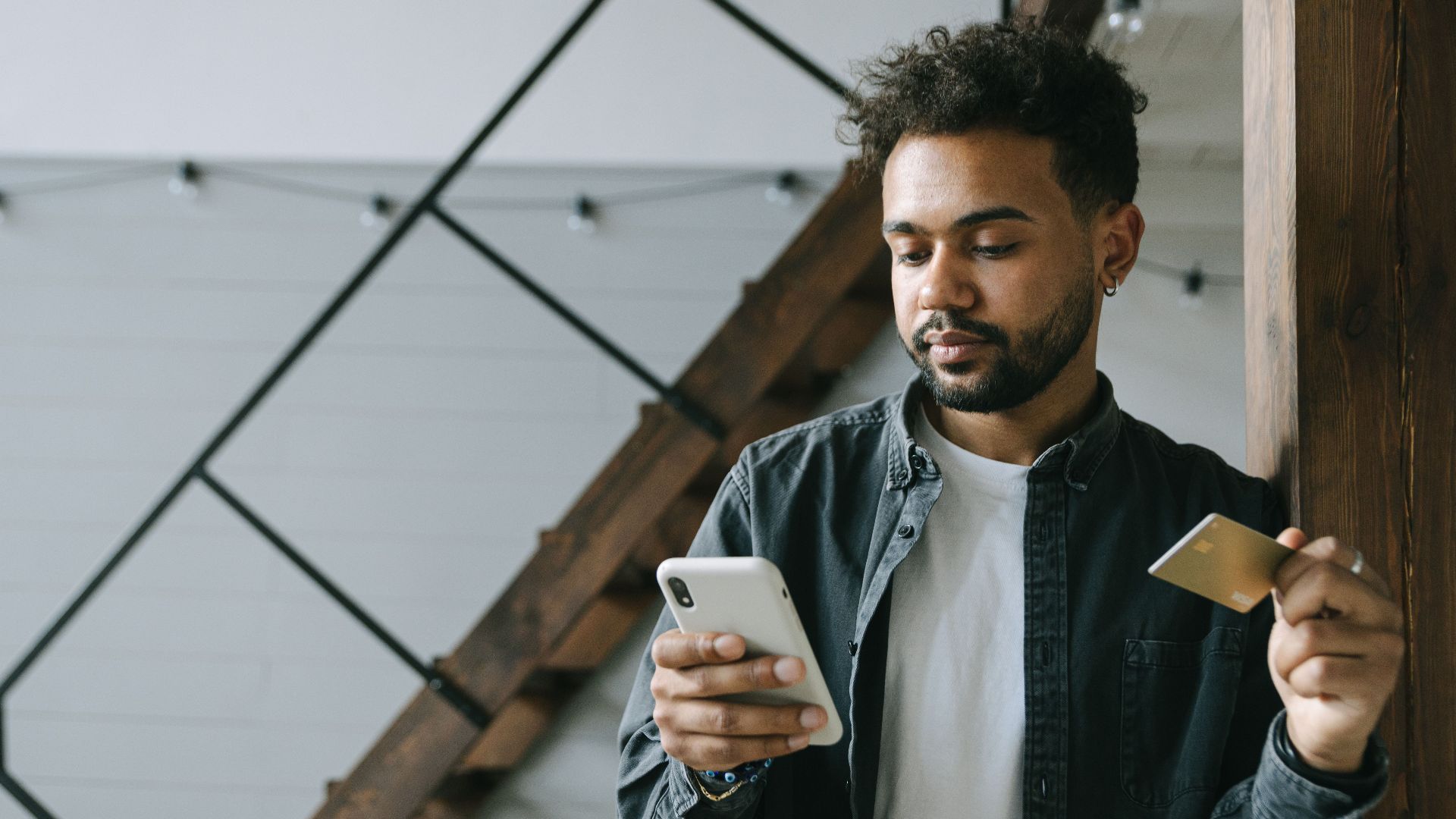 A young man using a smartphone and credit card for online shopping indoors.