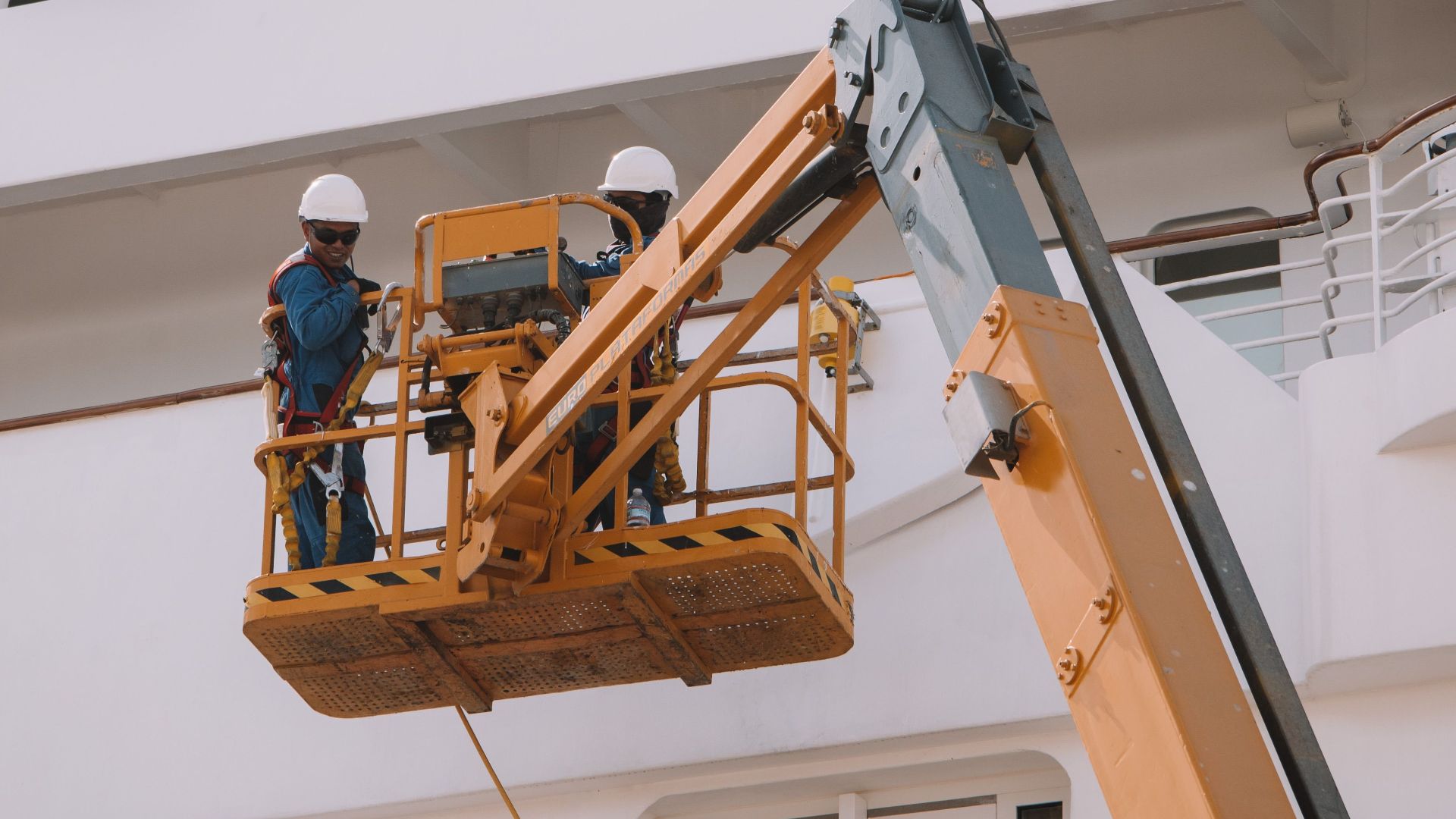 Two workers on a scissor lift performing maintenance on a cruise ship in Málaga, Spain.