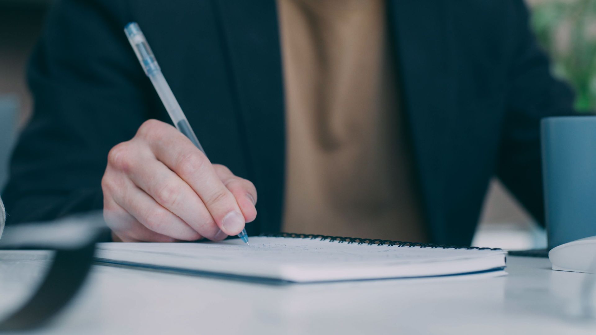 A person writing notes with a pen on a spiral notebook, indicating work or study.