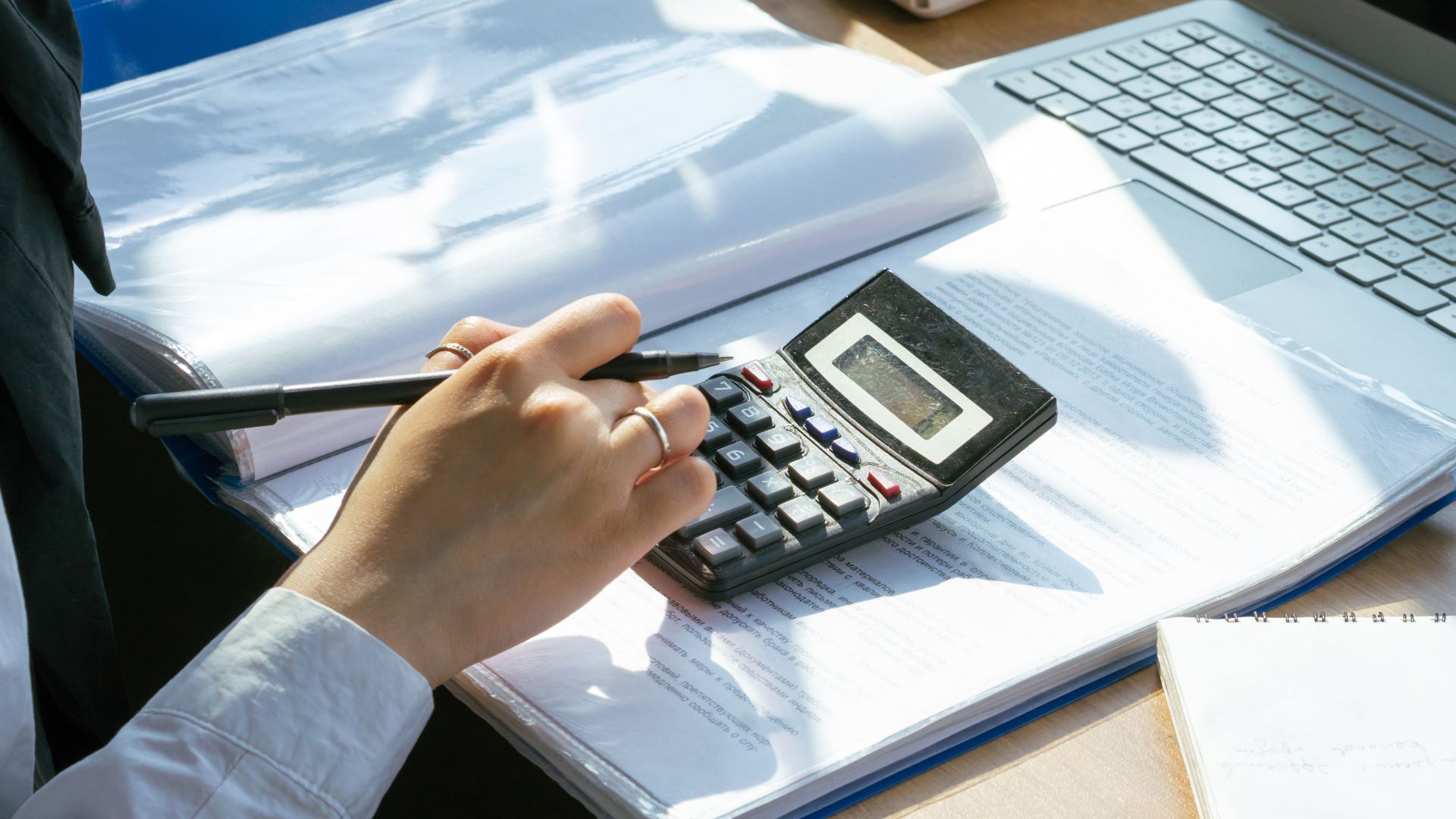 A person working on financial calculations using a calculator and laptop at an office desk.