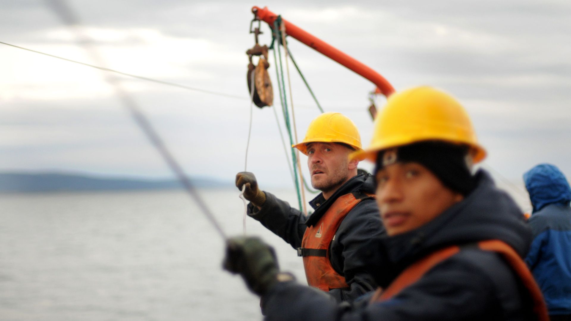Workers wearing safety gear secure equipment on a ship during the day.