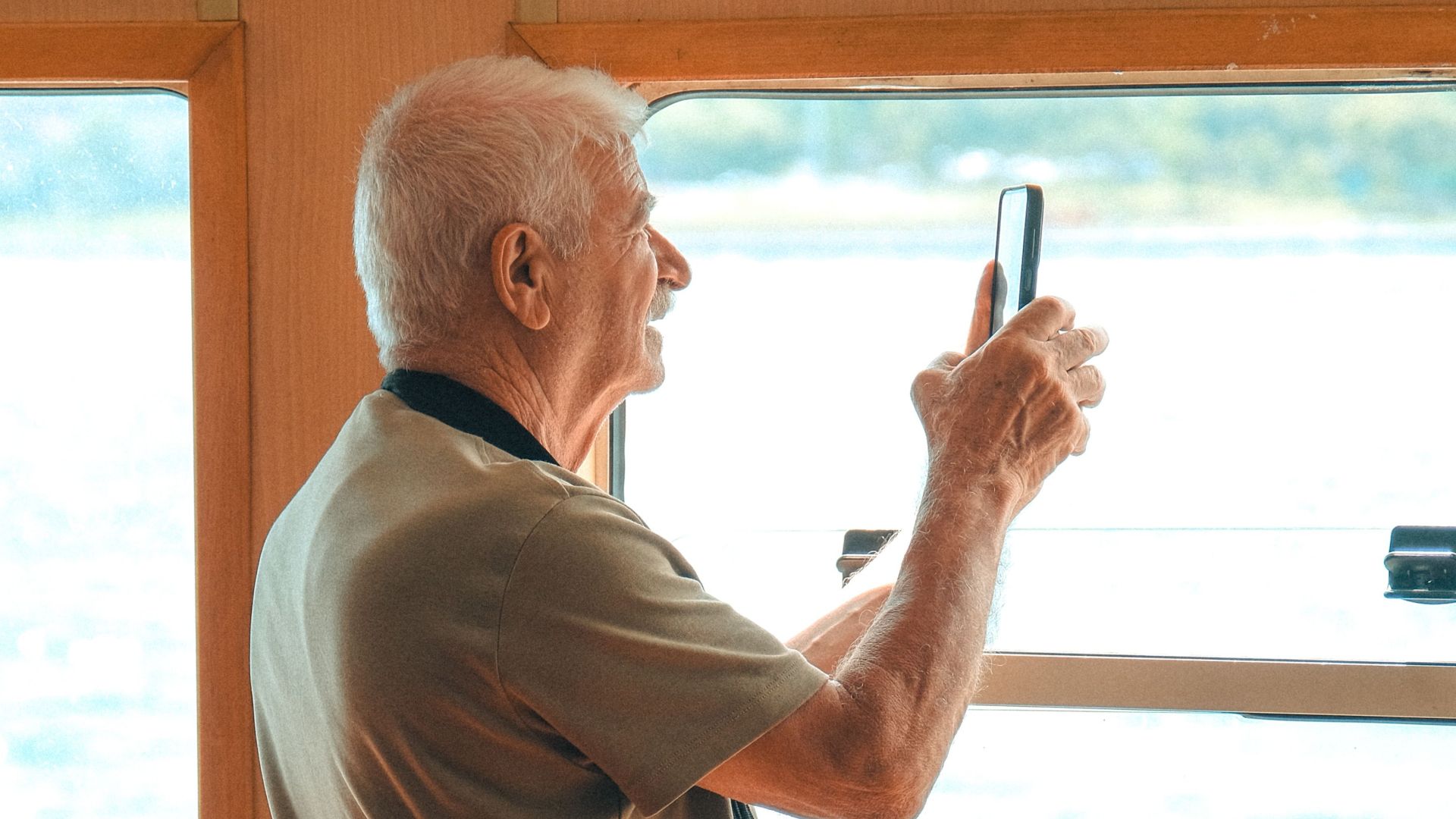 Elderly man taking a photo from a ferry window with his phone.