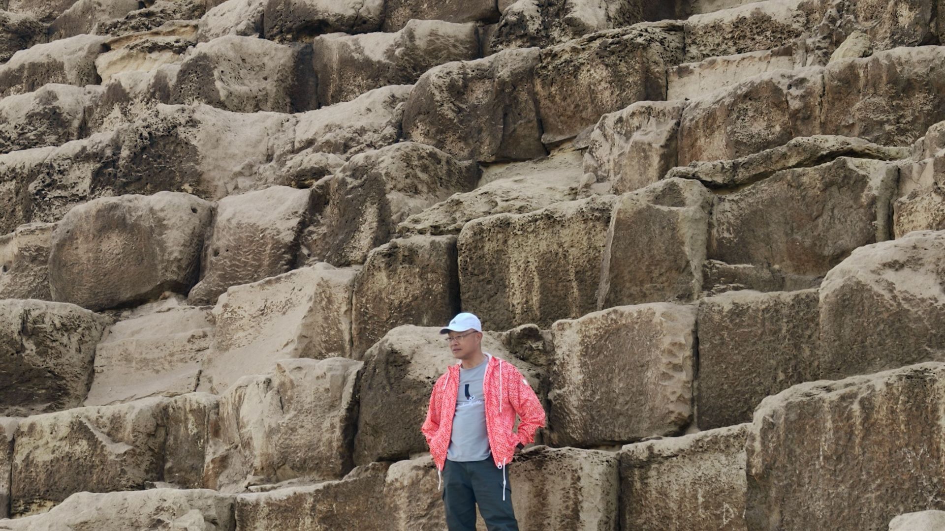 Tourist in vibrant attire stands on large stone blocks of the Giza Pyramid in Egypt.