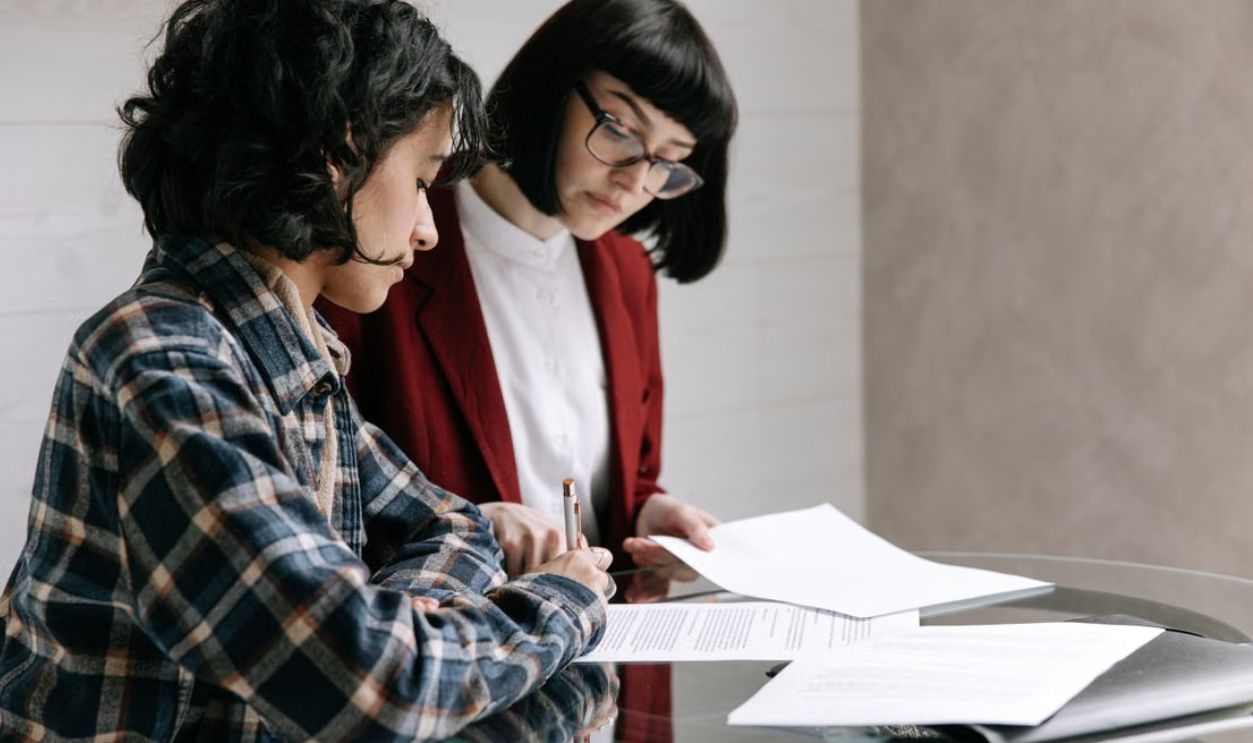 Two women reviewing and signing documents at an indoor glass table