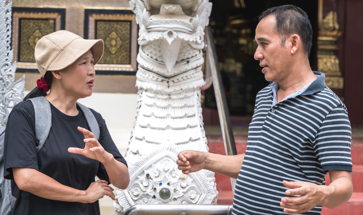 Local Asian male tour guide explaining temple history to Asian tourist woman