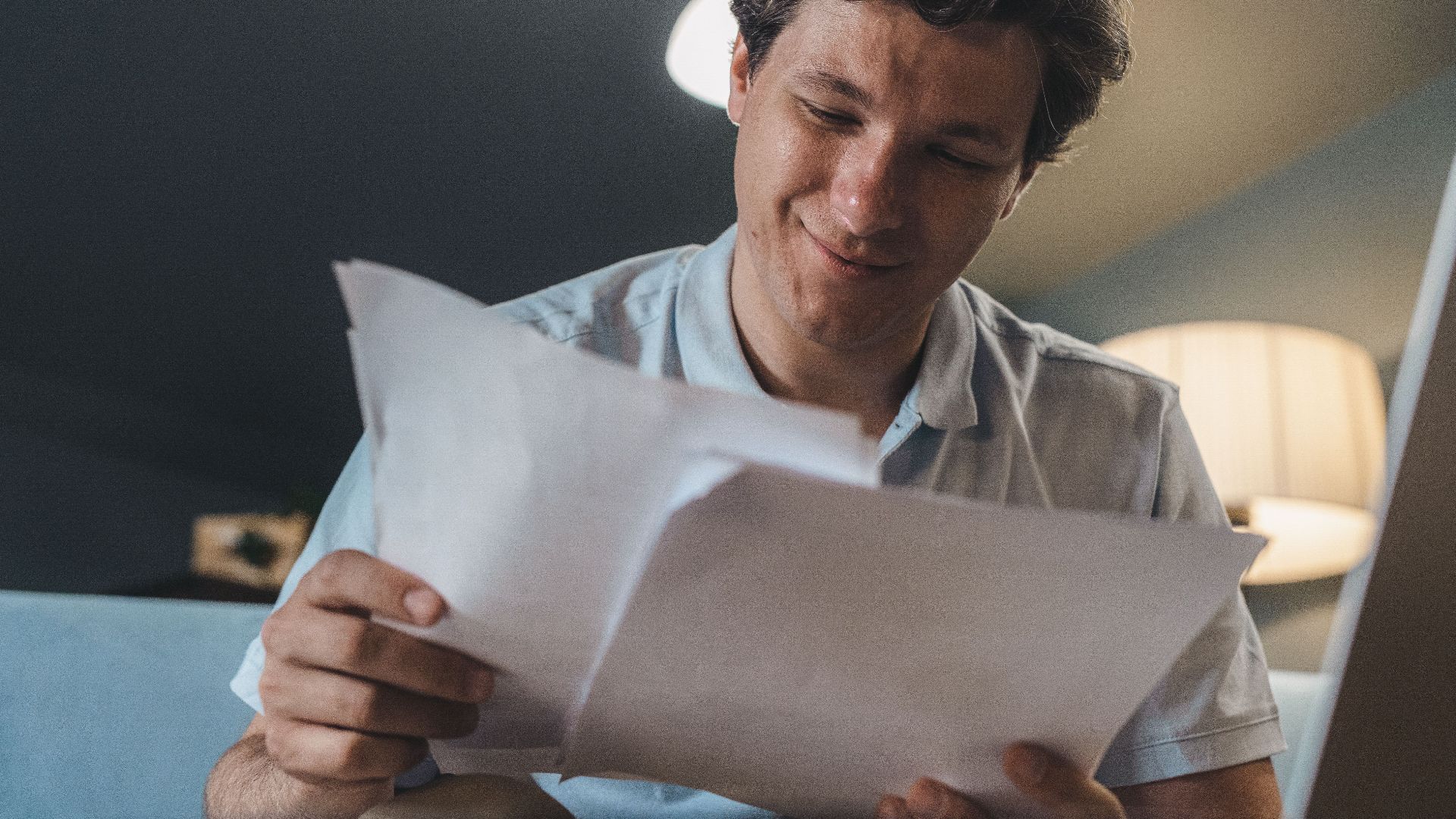 A cheerful man reading papers in a cozy indoor setting, radiating positivity.