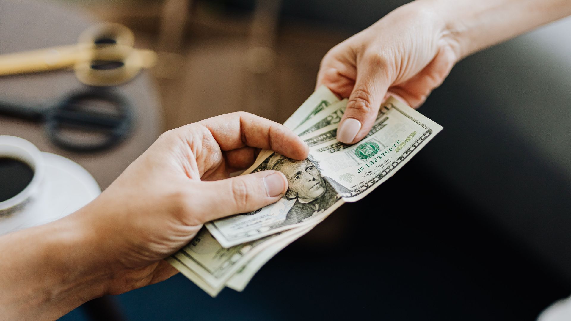 A close-up image of hands exchanging US dollar bills, symbolizing financial transaction or payment.