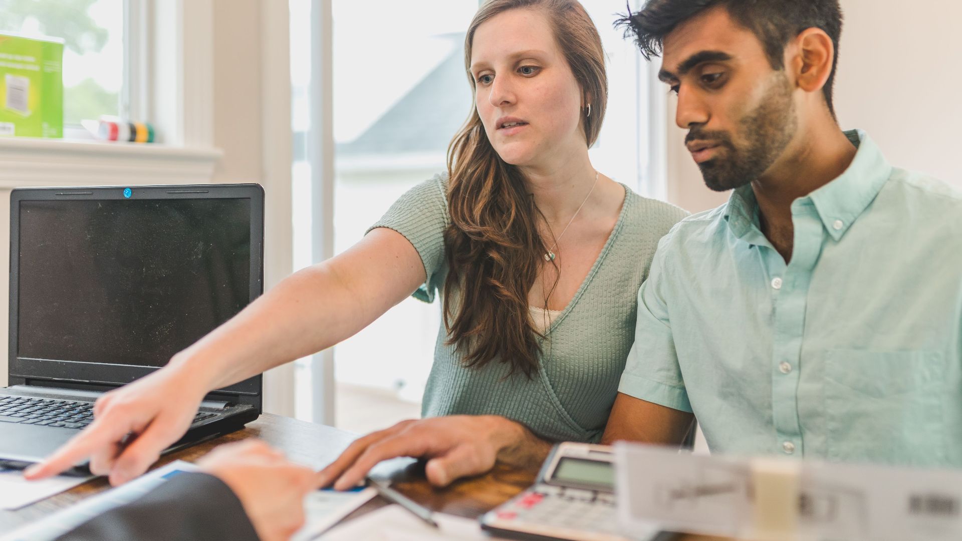 A young couple reviewing real estate documents with an advisor in a bright office.