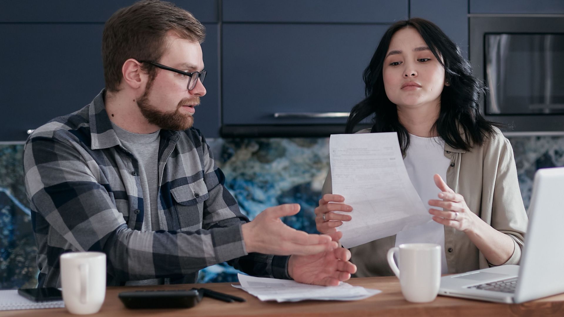 A couple having a discussion over financial documents at home with a laptop.
