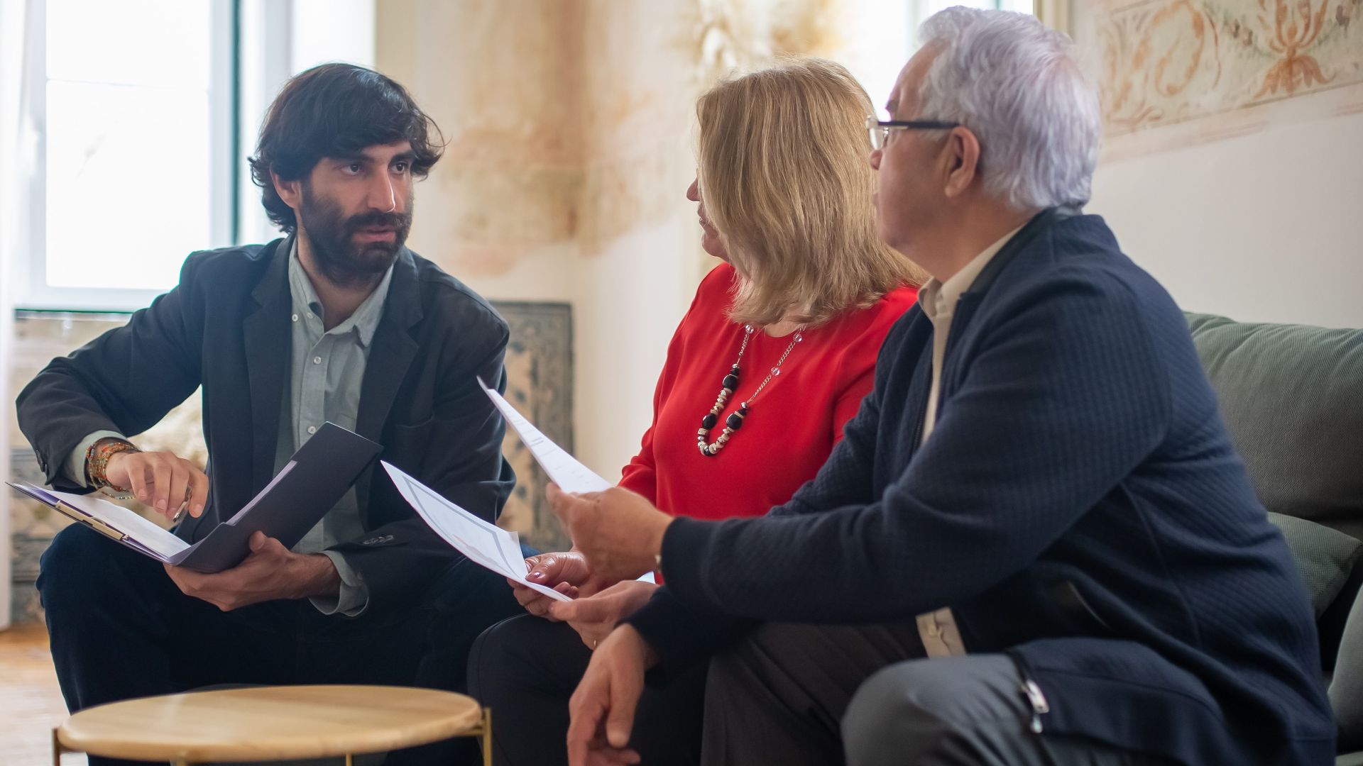 An advisor discussing financial documents with a senior couple indoors in a cozy living room setting.