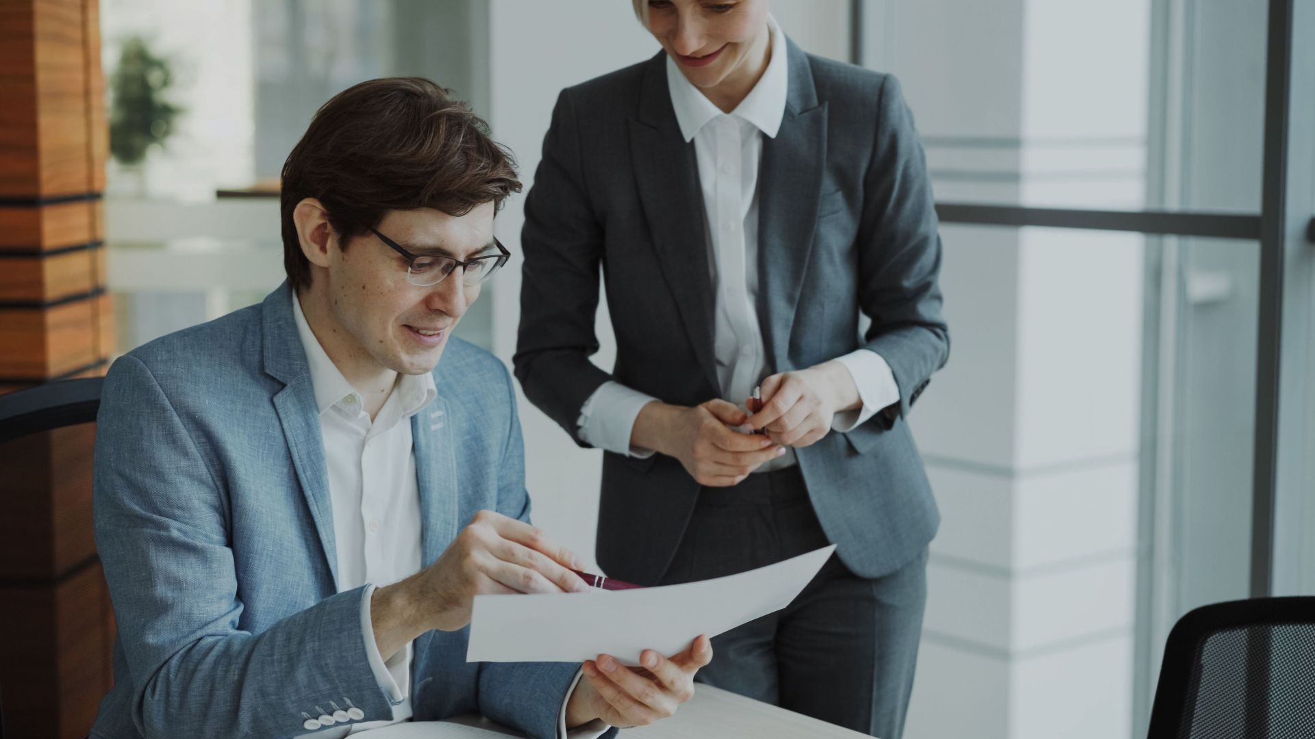 Two business professionals discussing a document in a modern office setting.