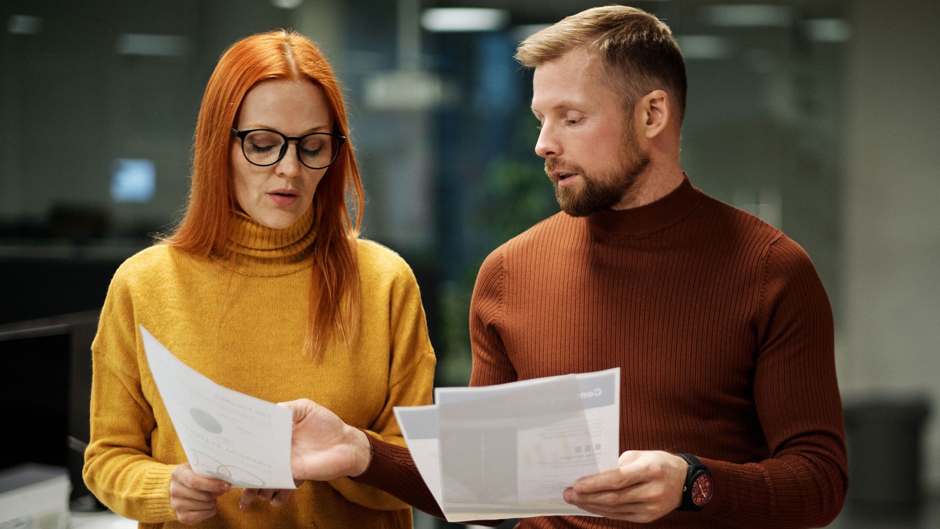 Two professionals in modern office discussing documents, reflecting collaboration and teamwork.