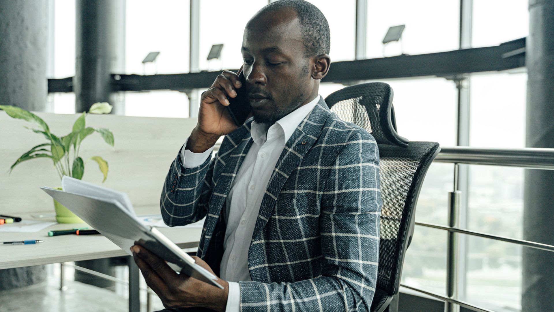 Professional businessman discussing documents during a phone call in a modern office setting.