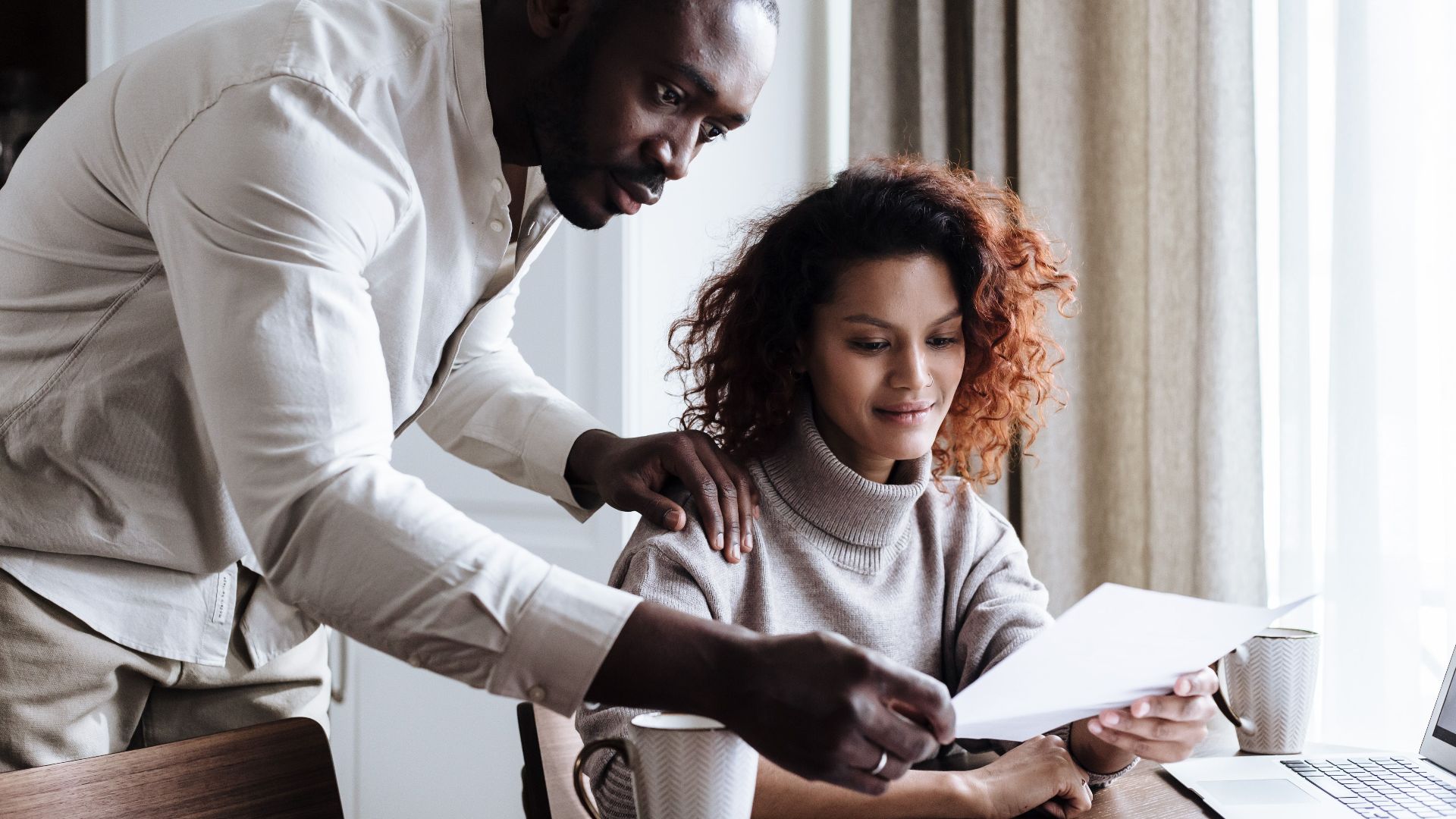 A couple working together at home, reviewing documents with a laptop and coffee.