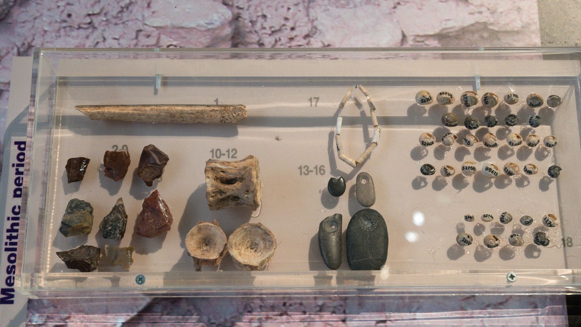 (1) Bone tool. (2-9) Flint tools. (10-12) tuna vertebrae. (13-16) Stone pendants. (17) Perforated shells. (18) Manufacturing stages of Cyclope neritea beads. Mesolithic, 7000 - 6000 BC. Findings from Franchthi Cave. Archaeological Museum of Nafplio.