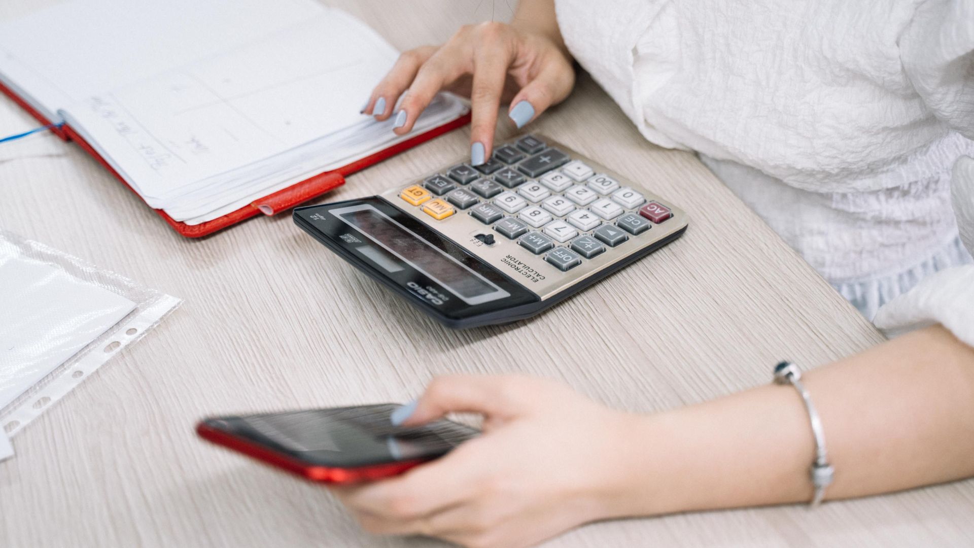 Close-up of a woman using a calculator and phone at her office desk.