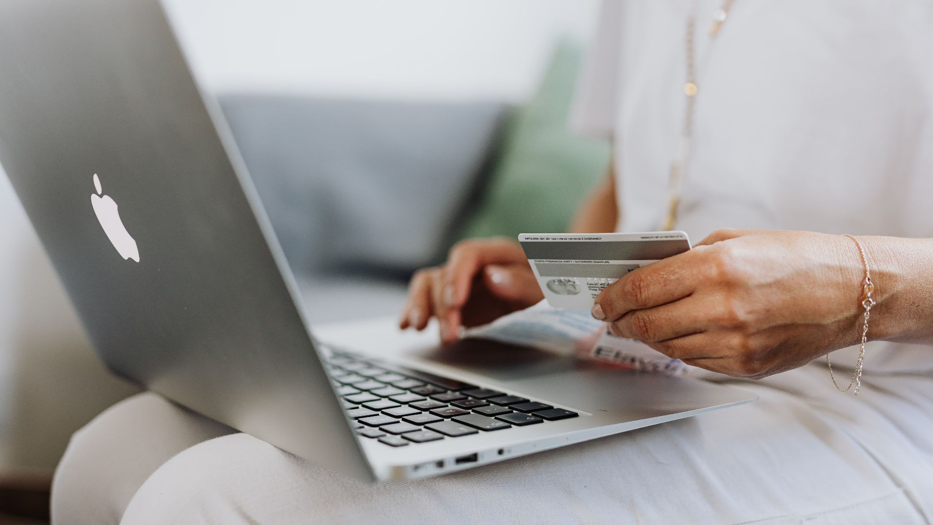 Close-up of a person holding a credit card while shopping online using a laptop at home.