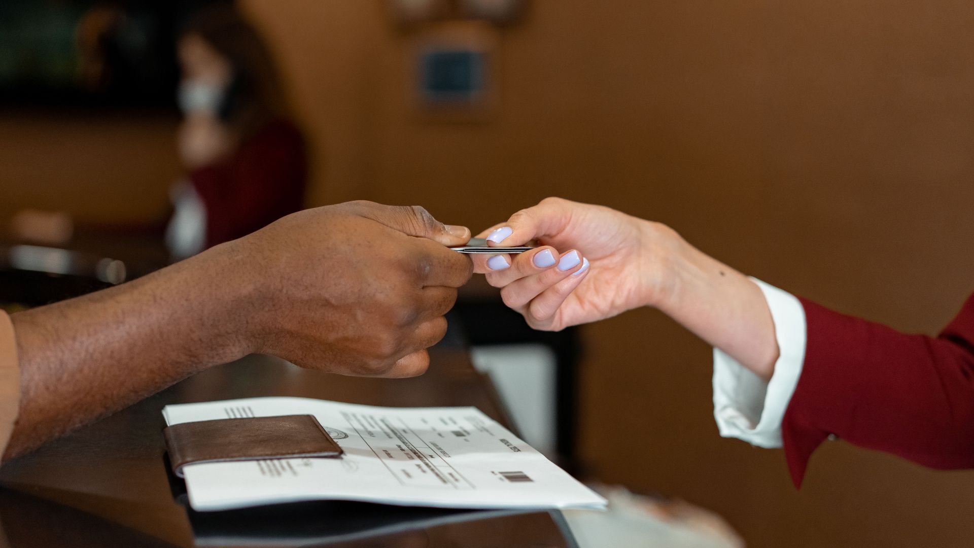 Close-up of a hotel receptionist receiving a credit card from a guest, highlighting a transaction at check-in.