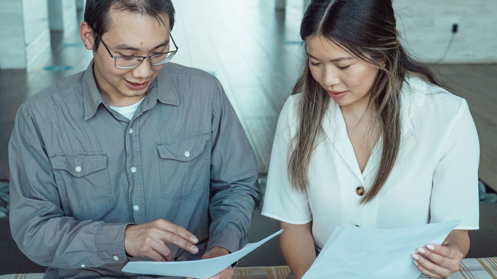 Two coworkers reviewing documents in a modern office, focused on teamwork and planning.