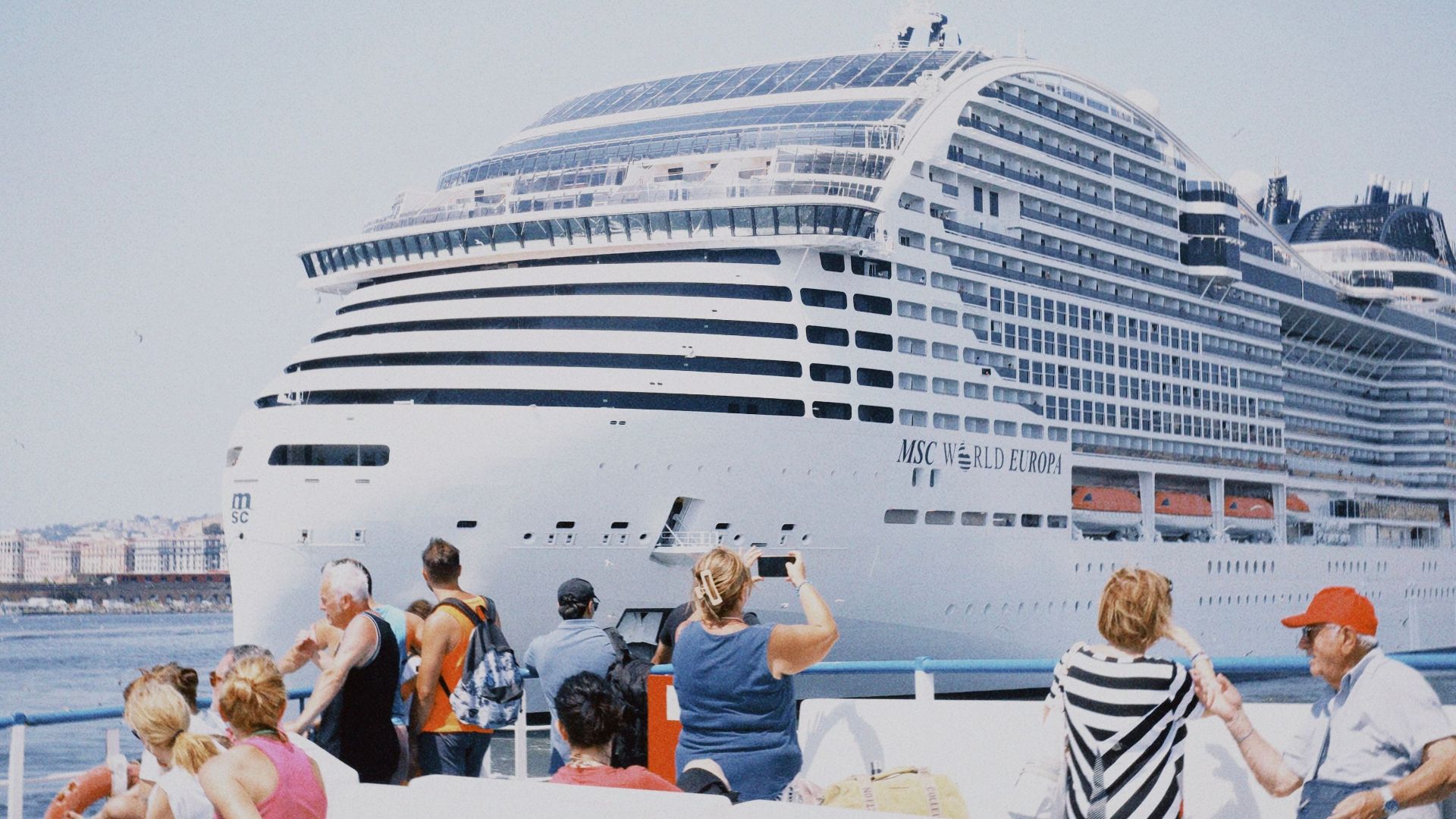Tourists watch MSC World Europa cruise ship at sea on a sunny day.